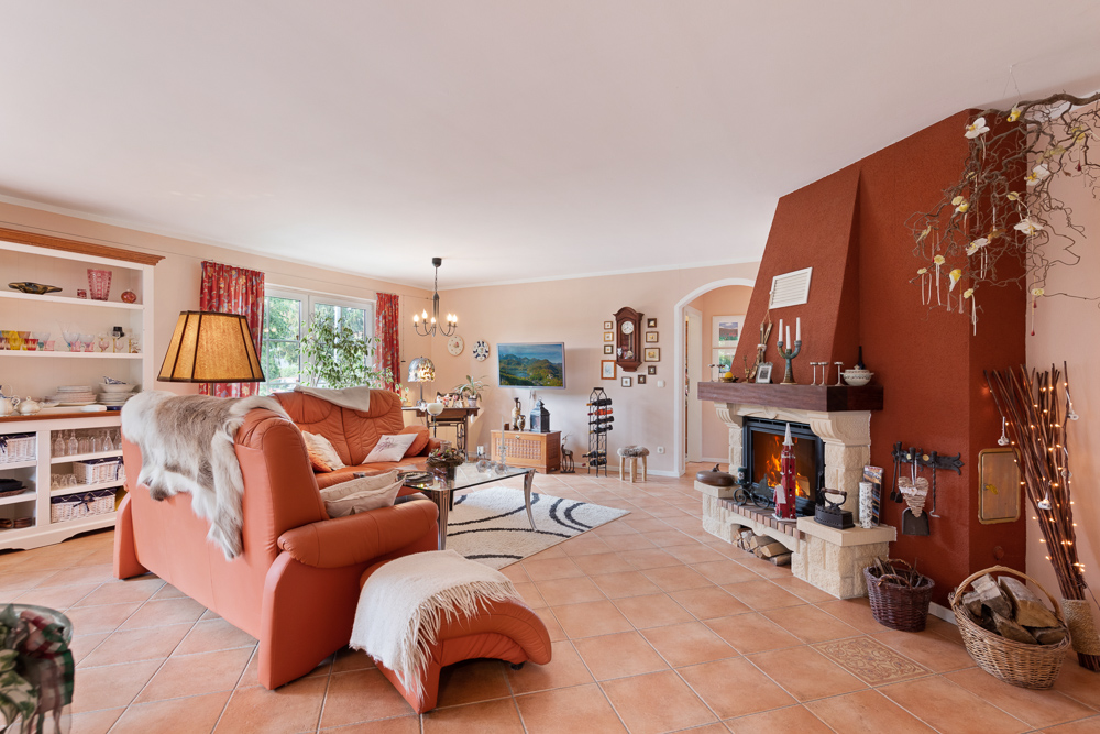 Gemütliches Wohnzimmer mit Kamin, roten Sofas, Teppich und großen Fenstern.
