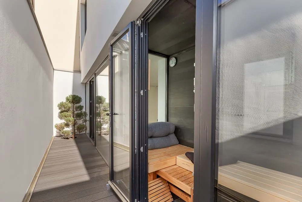 Schmaler Balkon mit Holzboden, Glasfront und geöffneter Tür zu einer Sauna mit Holzbänken.