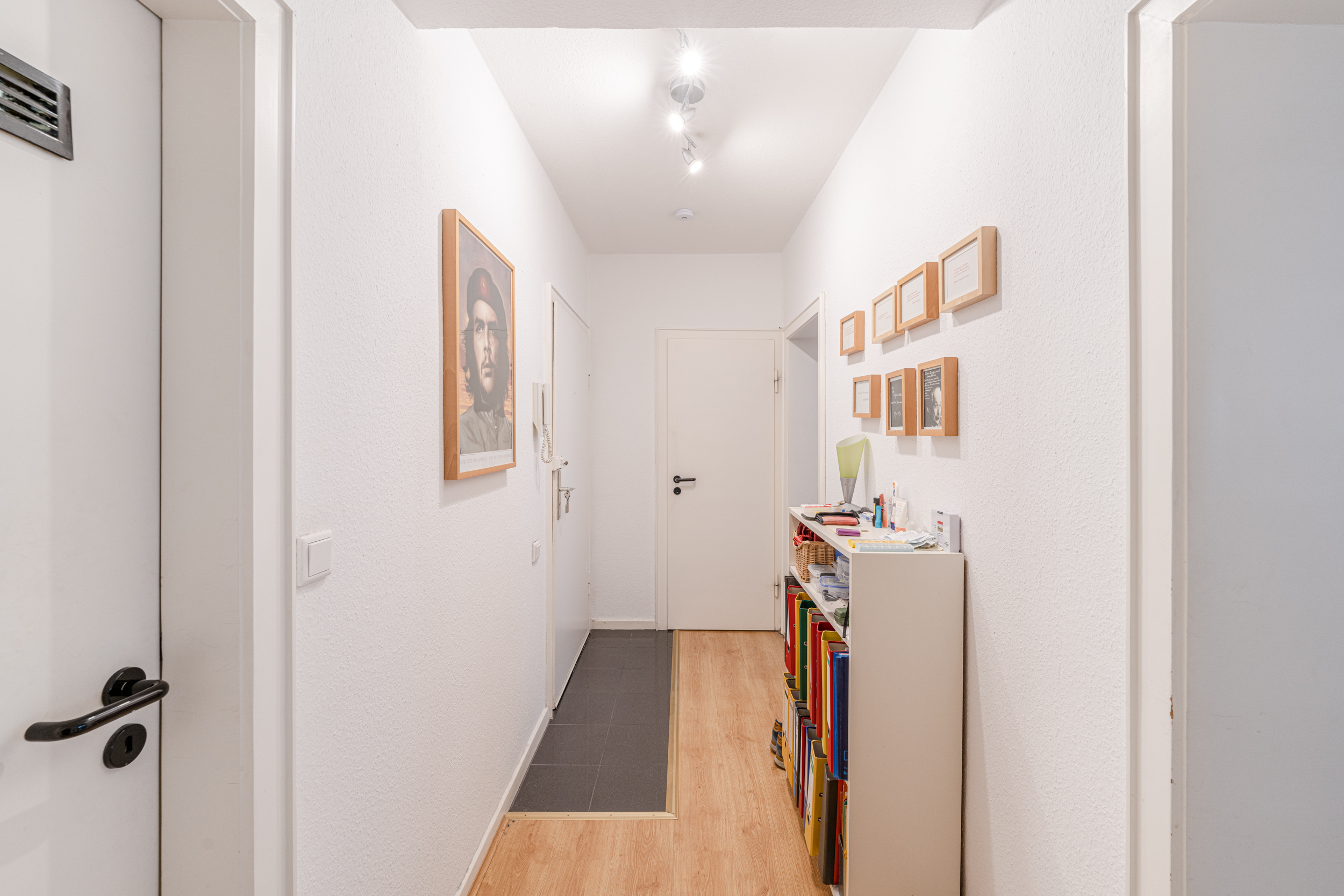 Heller Flur mit Holzfußboden, Regal, Bilderrahmen und einem großen Poster an der Wand.