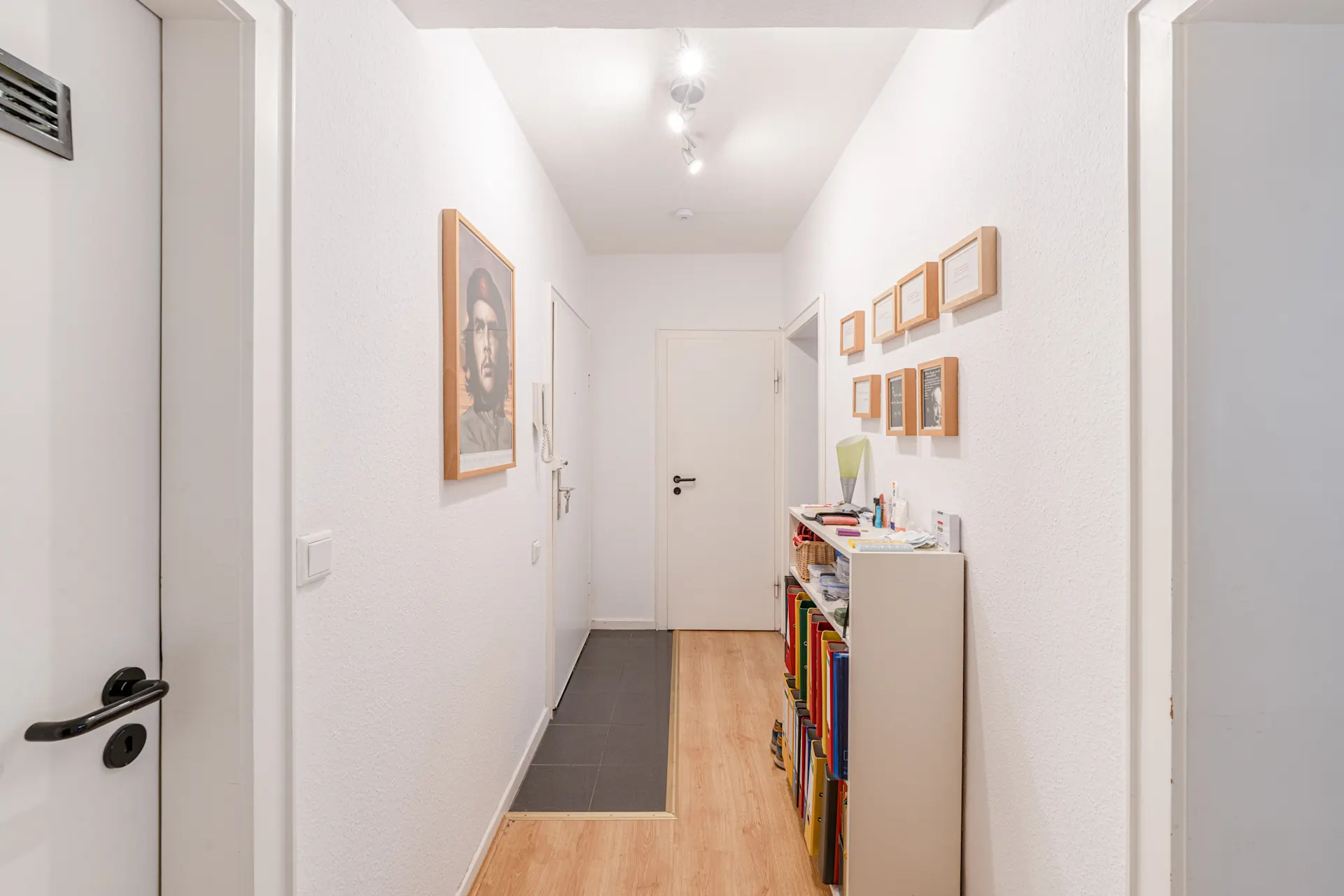 Heller Flur mit Holzfußboden, Regal, Bilderrahmen und einem großen Poster an der Wand.