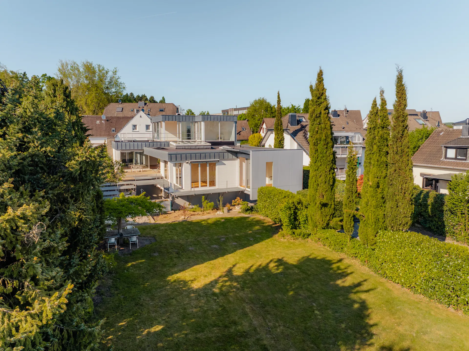 Modernes Haus mit großem Garten, umgeben von Bäumen und weiteren Wohnhäusern.