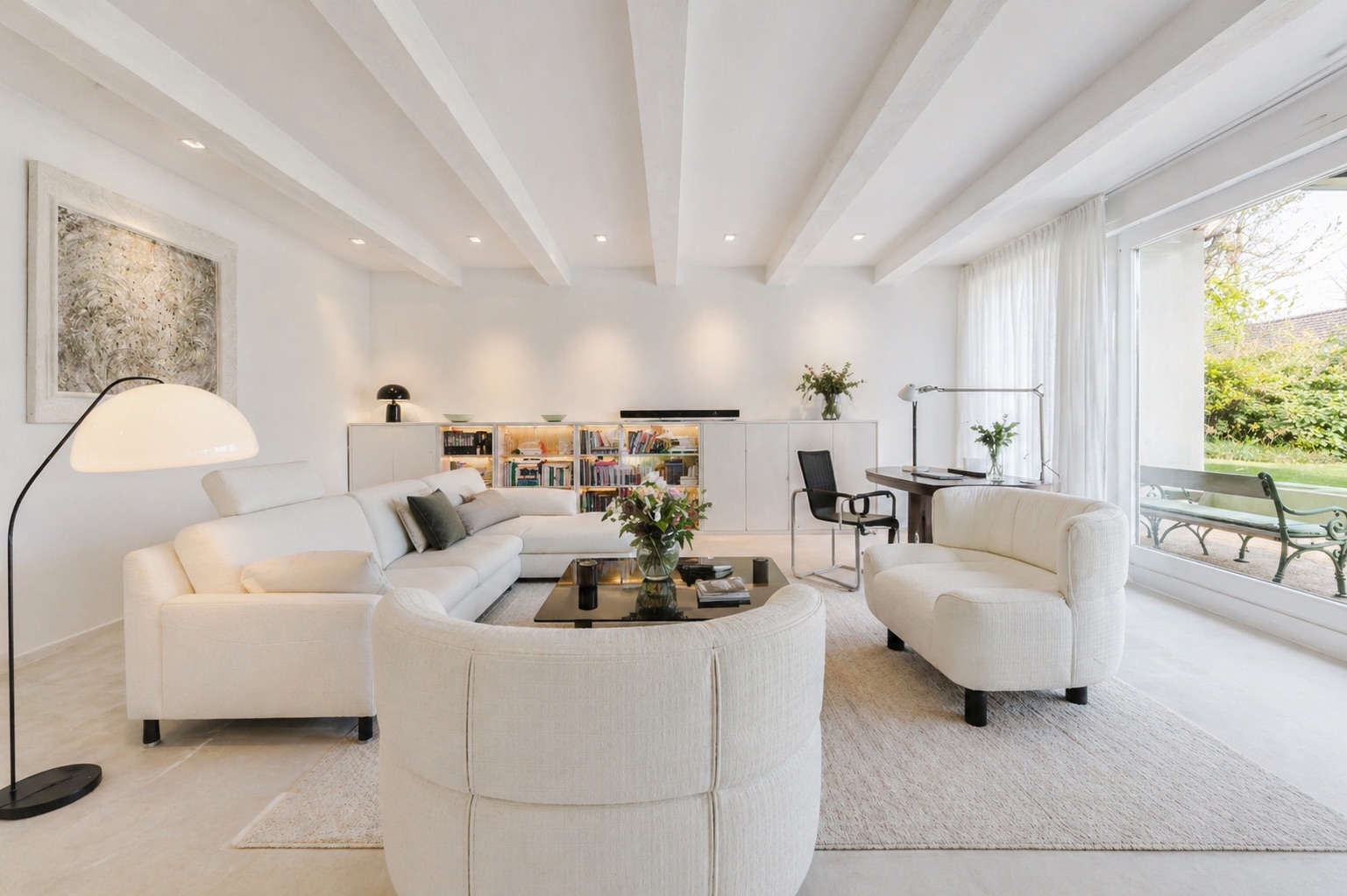 Helles Wohnzimmer mit weißen Sofas, Couchtisch, Regal, Schreibtisch und großem Fenster zum Garten.