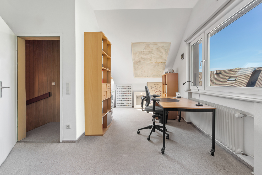 Helles Arbeitszimmer mit großem Fenster, Schreibtisch, Bürostuhl und Regal.