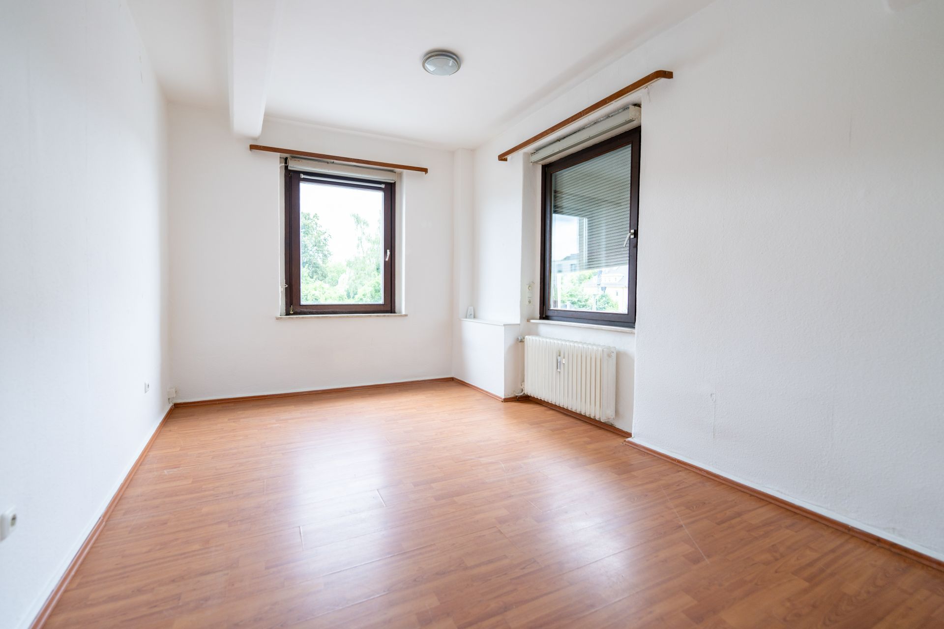 Leeres Zimmer mit weißer Wand, zwei Fenstern und Holzfußboden.