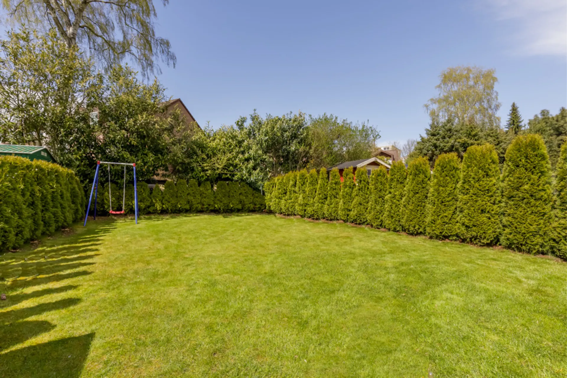 Garten mit grünem Rasen, Hecken und einer Schaukel im linken Bereich.