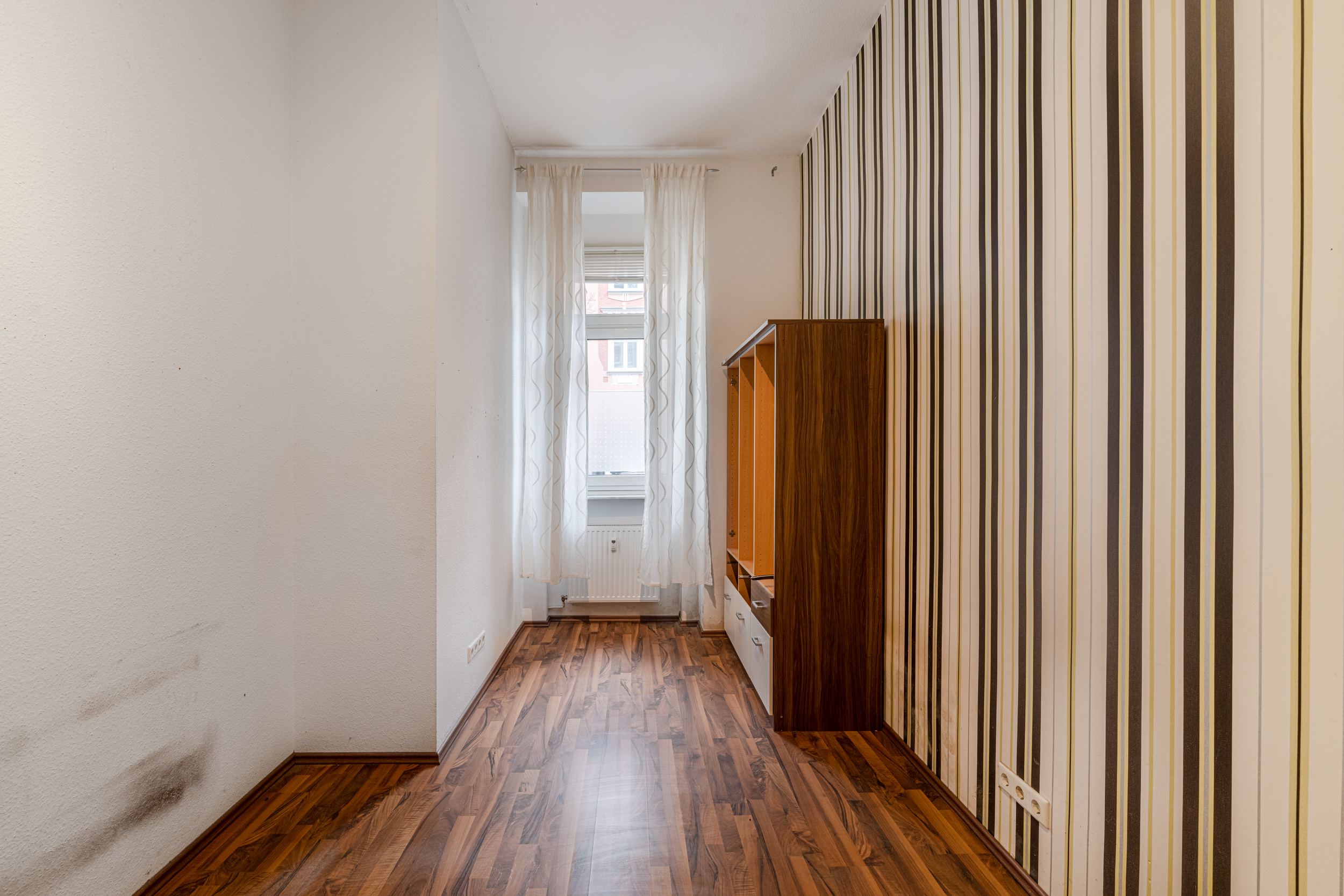 Schmaler Raum mit Holzfußboden, gestreifter Tapete, Fenster und Schrank auf der rechten Seite.