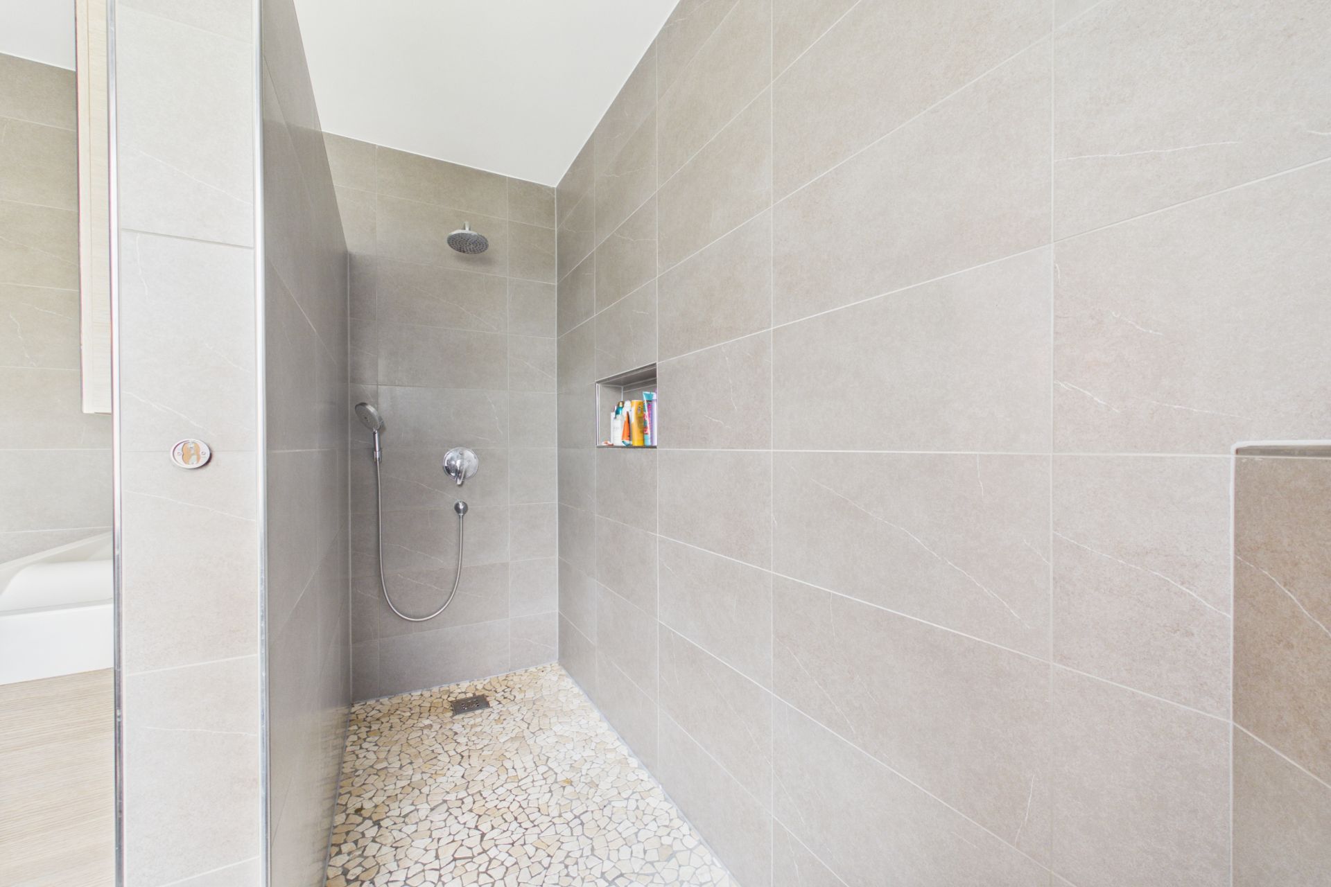Begehbare Dusche mit grauen Fliesen und eingelassenem Regal in der Wand.