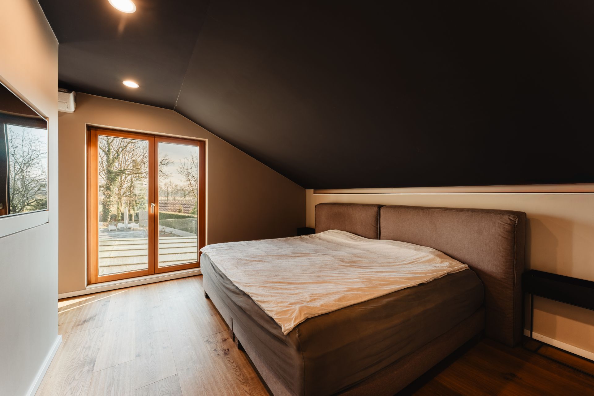 Schlafzimmer mit großem Bett und Dachschräge, Holzboden und Glastüren zum Balkon.