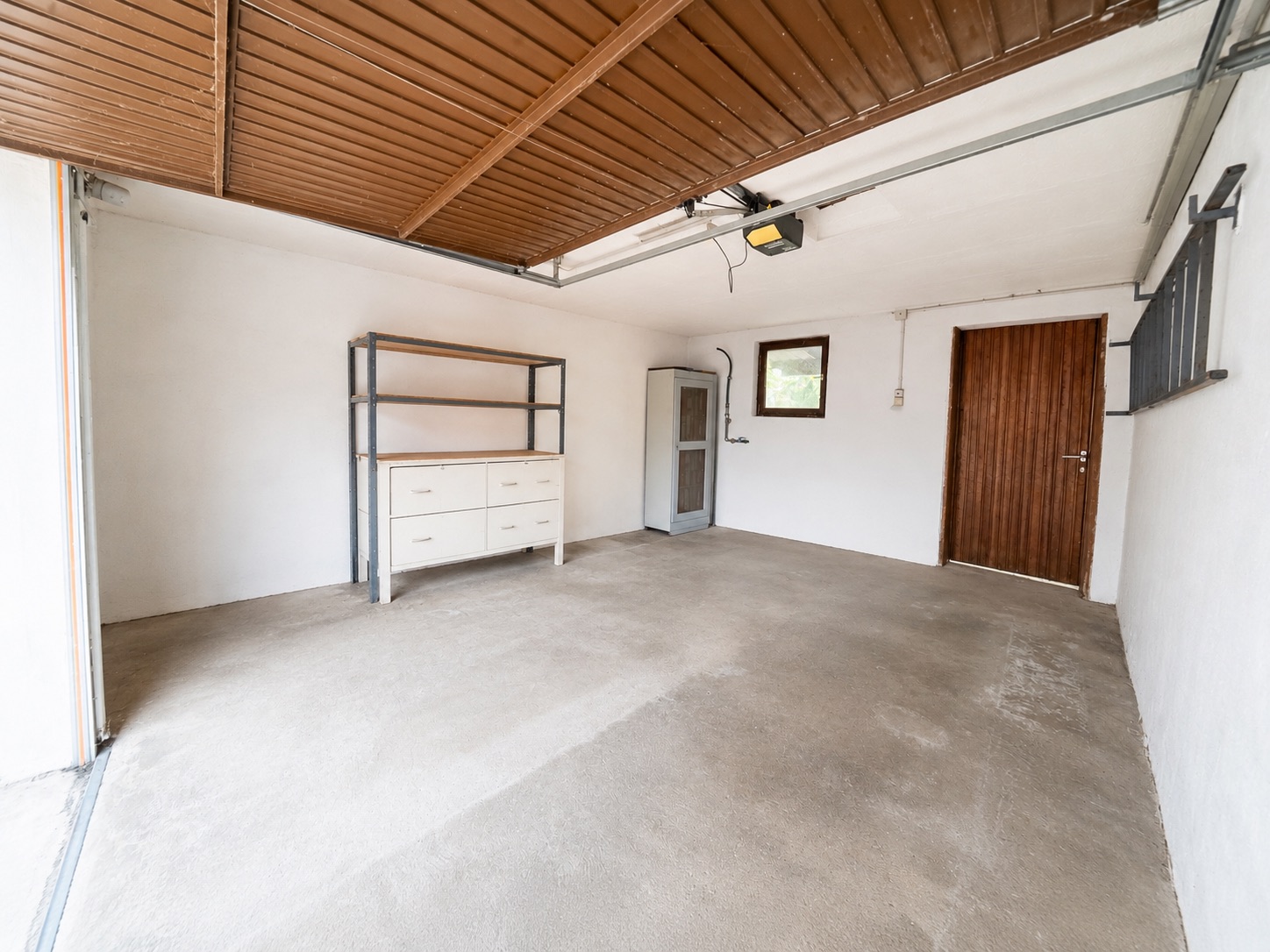 Leere Garage mit Regal, Kommode, Holztür und kleinem Fenster.