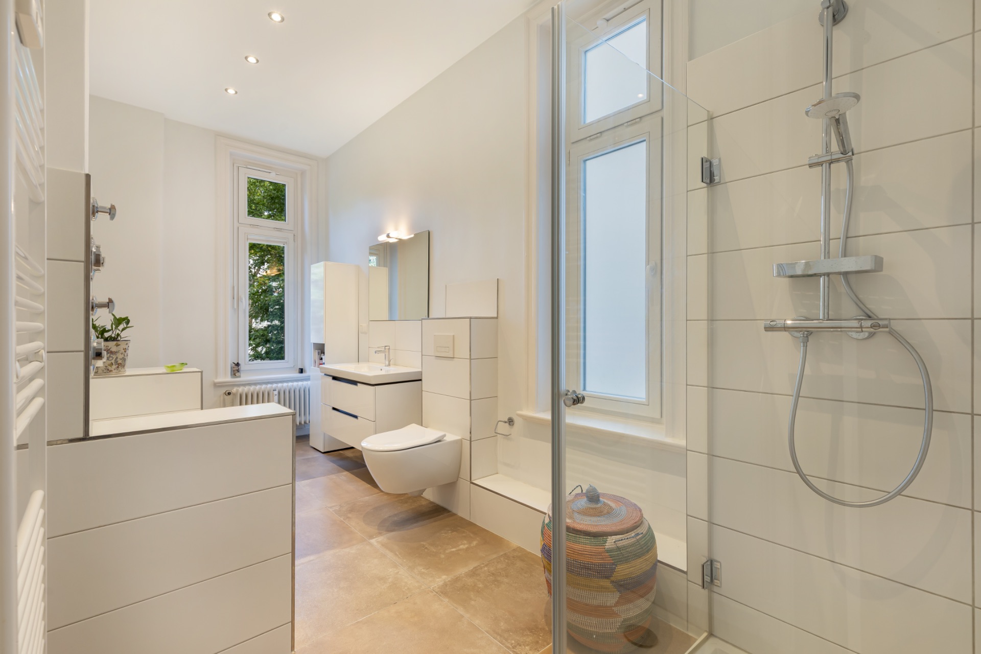 Modernes Badezimmer mit ebenerdiger Dusche, Hänge-WC, Waschbecken und großem Fenster.