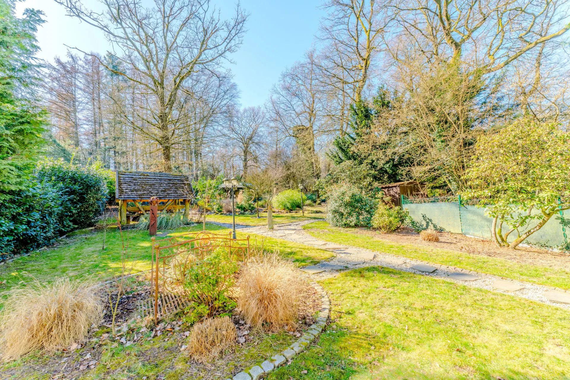 Großer Garten mit Rasen, Bäumen, Sträuchern, Wegen und einer Holzüberdachung.