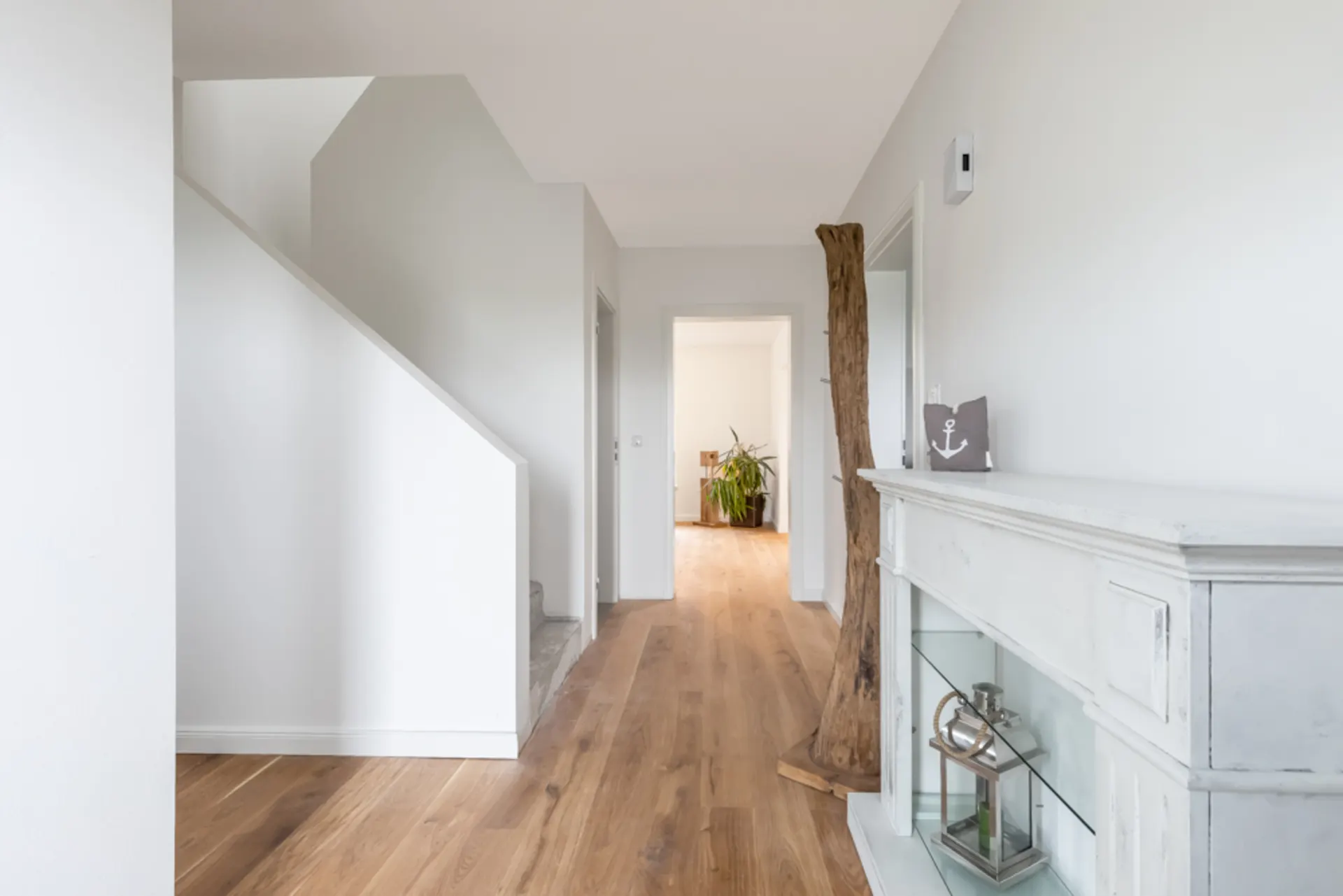 Heller Flur mit Holzfußboden, Treppe, Pflanzen und Dekoration auf einem weißen Kamin.