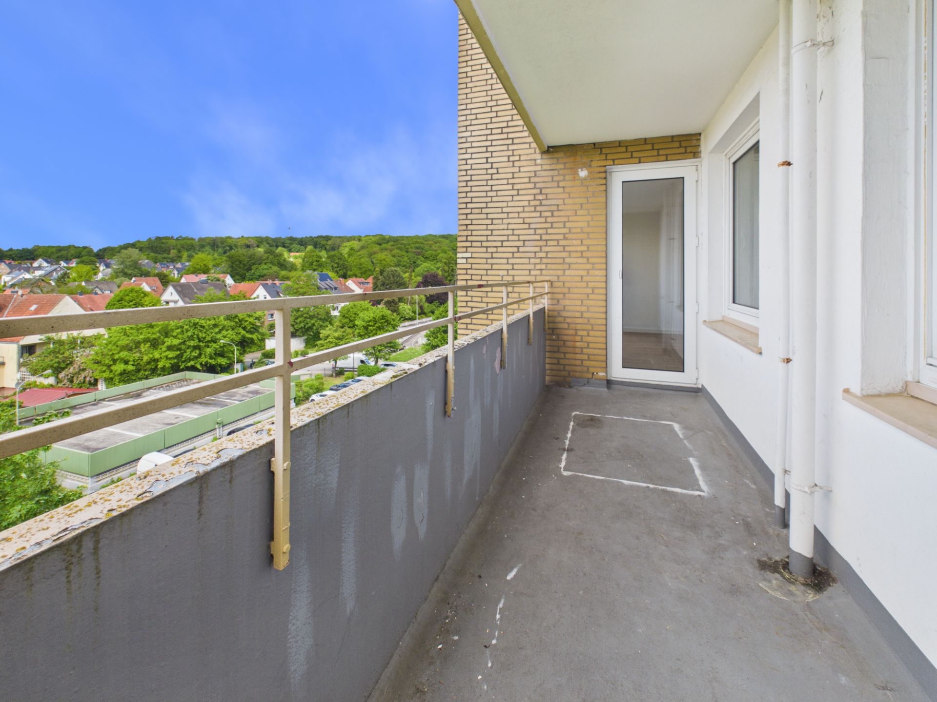 Langer Balkon mit Geländer und Blick auf grüne Umgebung, Zugang durch Glastür.