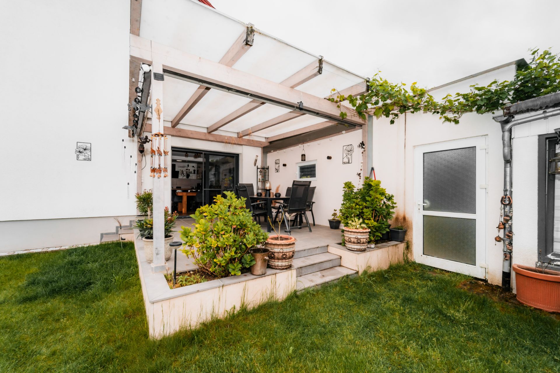 Überdachte Terrasse mit Sitzgruppe, Pflanzen und direktem Zugang zum Garten.