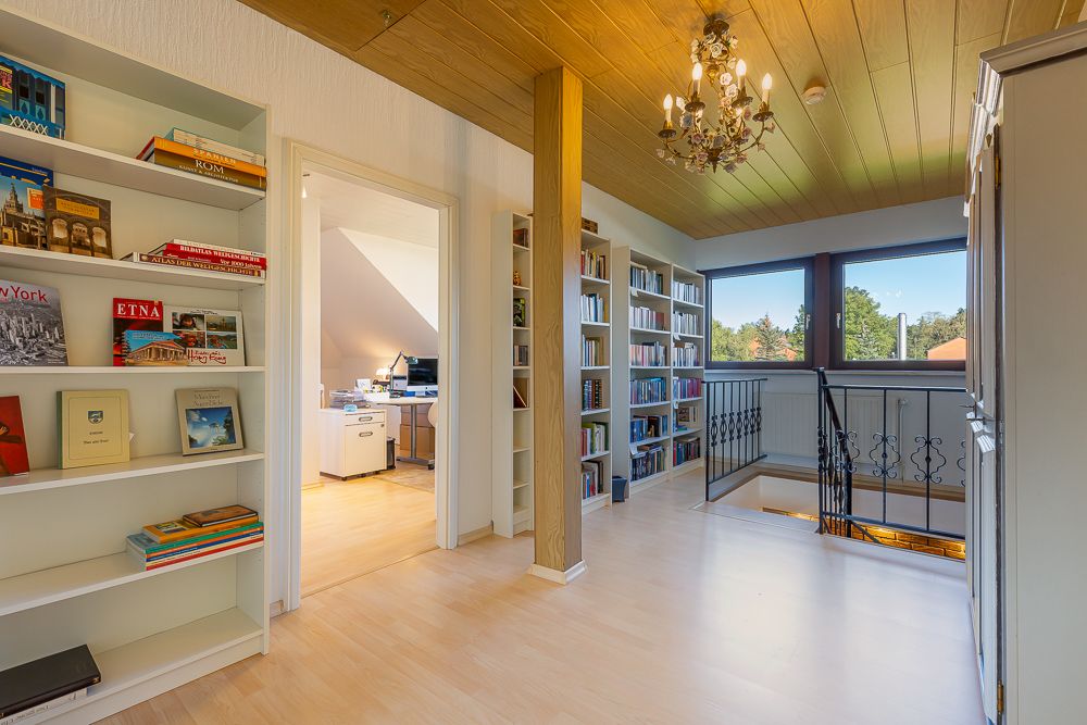 Heller Flur mit Bücherregalen, großer Fensterfront, Treppe und Zugang zu einem Arbeitszimmer.