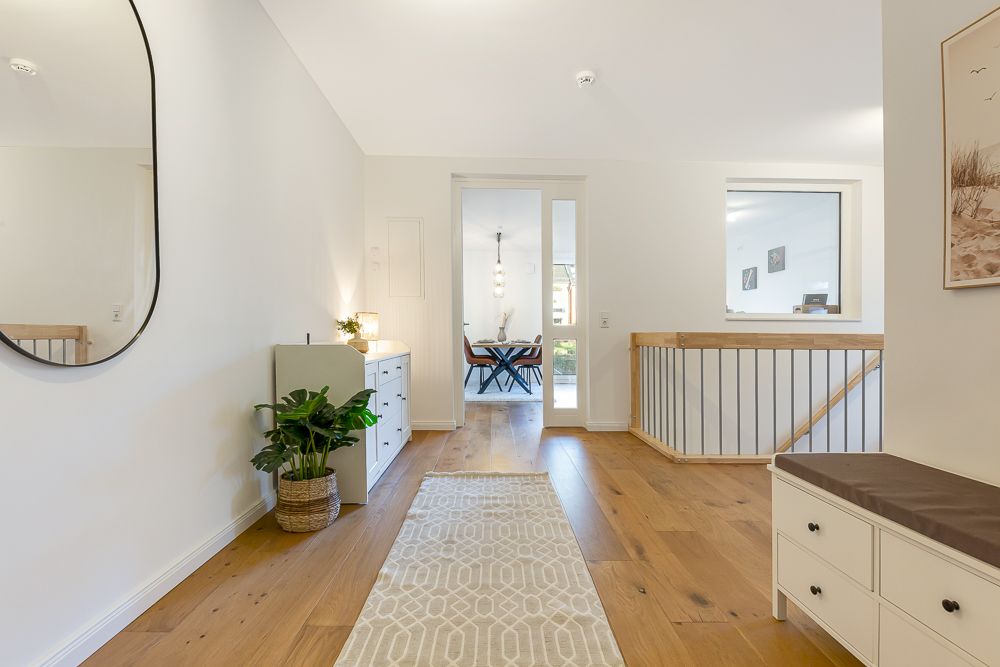 Heller Flur mit Holzfußboden, Spiegel, Kommode, Pflanze und Blick in ein Esszimmer.