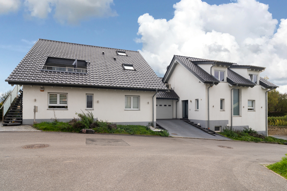 Zwei moderne Wohnhäuser mit grauen Dächern und Garage an einer Straße.