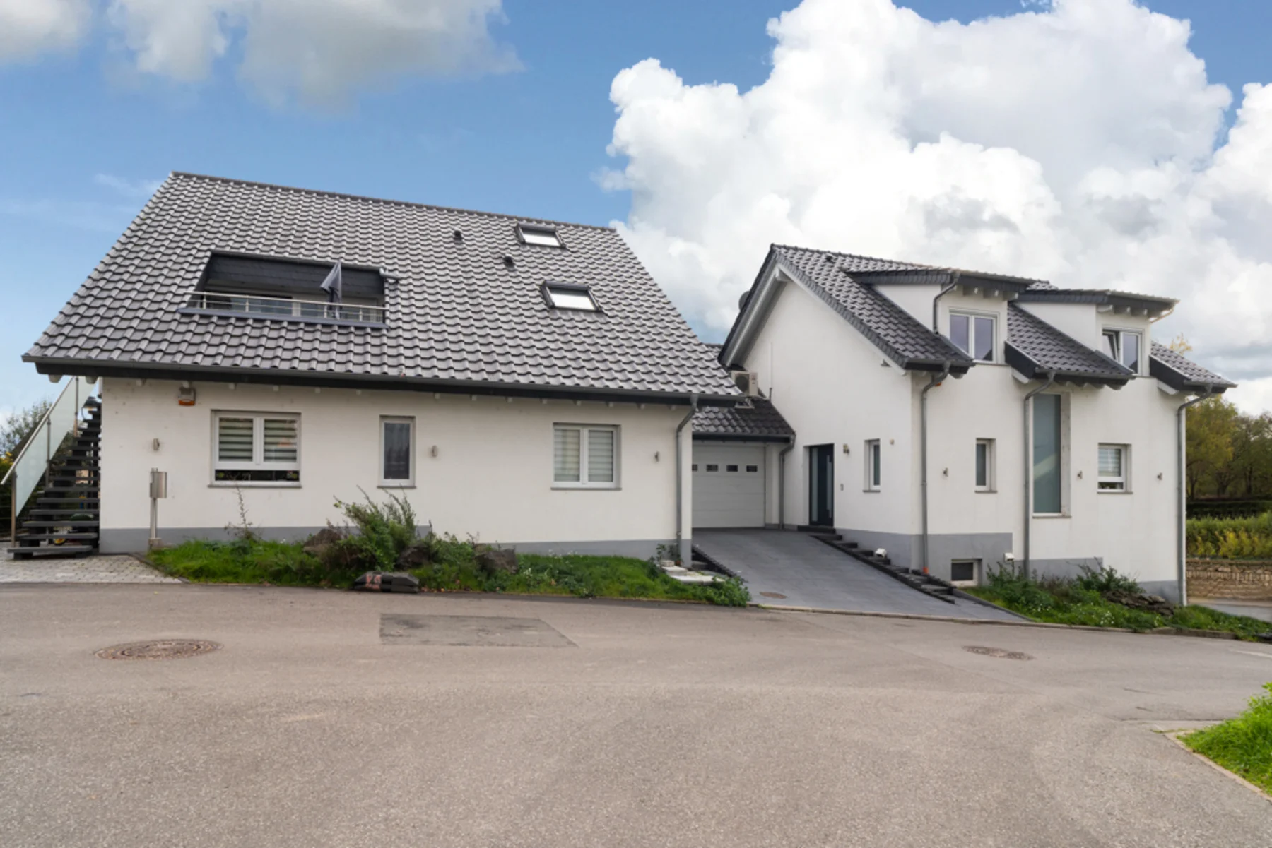 Zwei moderne Wohnhäuser mit grauen Dächern und Garage an einer Straße.