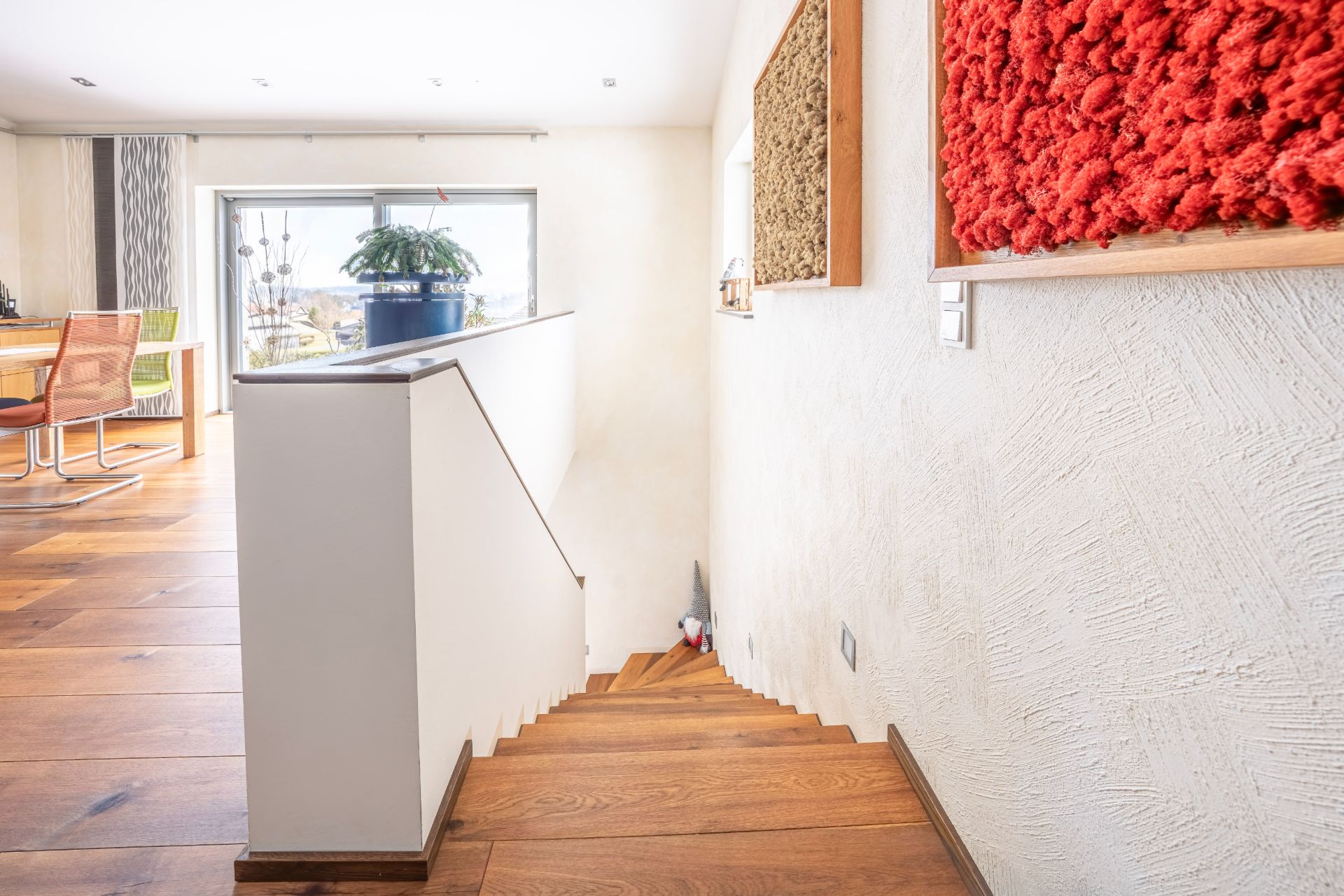 Helle Treppe mit Holzstufen, Blick ins Wohnzimmer mit Stühlen und großem Fenster.