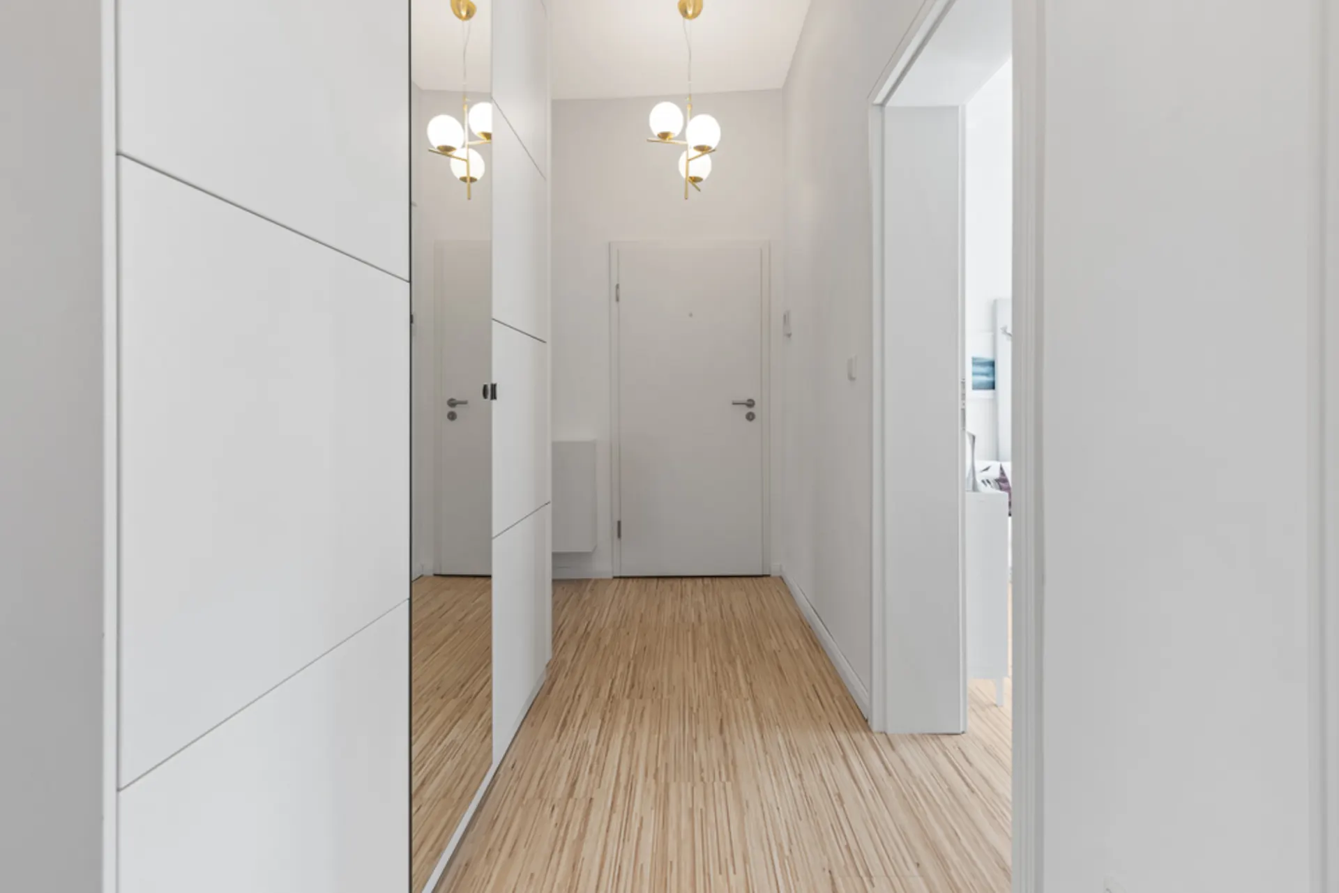Heller Flur mit Holzboden, weißen Wänden, Spiegel und moderner Deckenleuchte.
