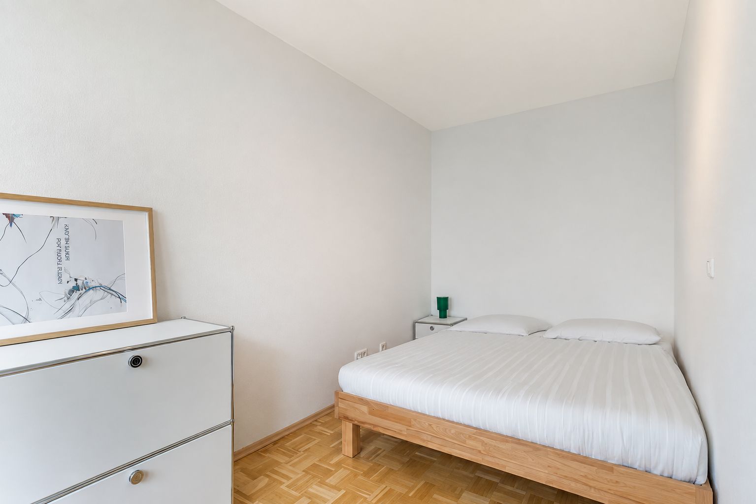 Helles Schlafzimmer mit Doppelbett, weißem Schrank und einem Bild an der Wand.