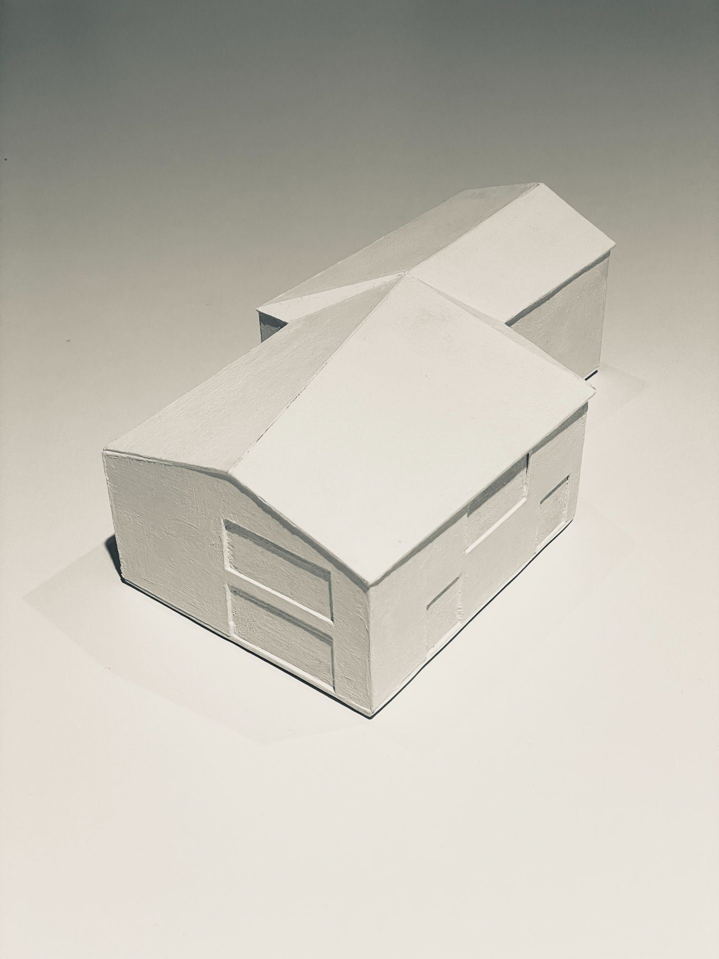 Weißes Architekturmodell mit zwei verbundenen Gebäudeteilen und Satteldächern.
