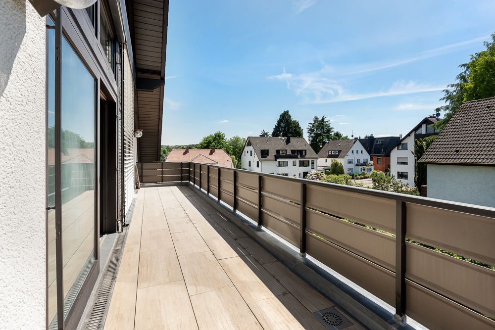 Großer Balkon mit Blick auf Nachbarhäuser und blauen Himmel.