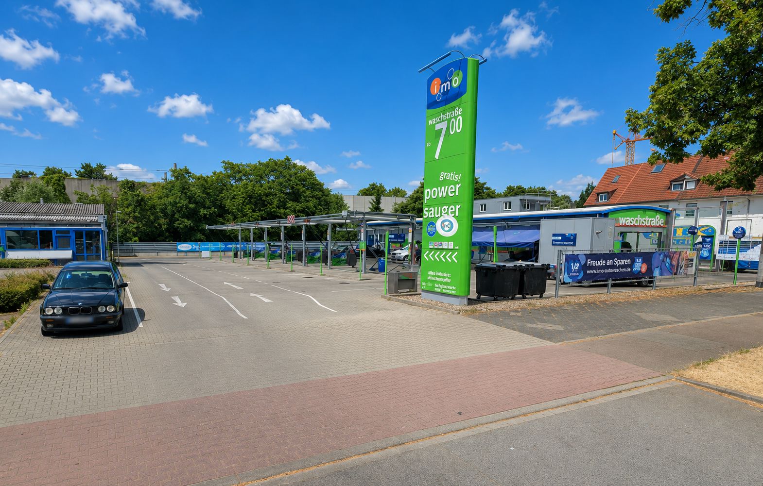 Offene Autowaschanlage mit einem geparkten Auto und grünem Preisschild im Vordergrund.