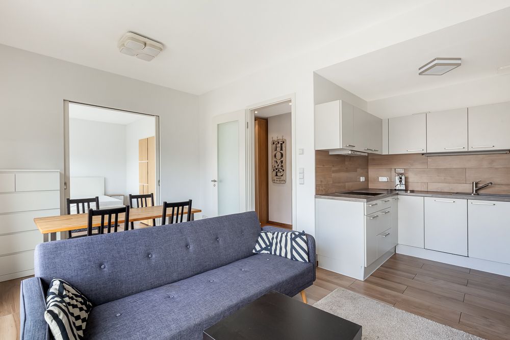 Modernes Wohnzimmer mit grauem Sofa, Esstisch und offener weißer Küche.