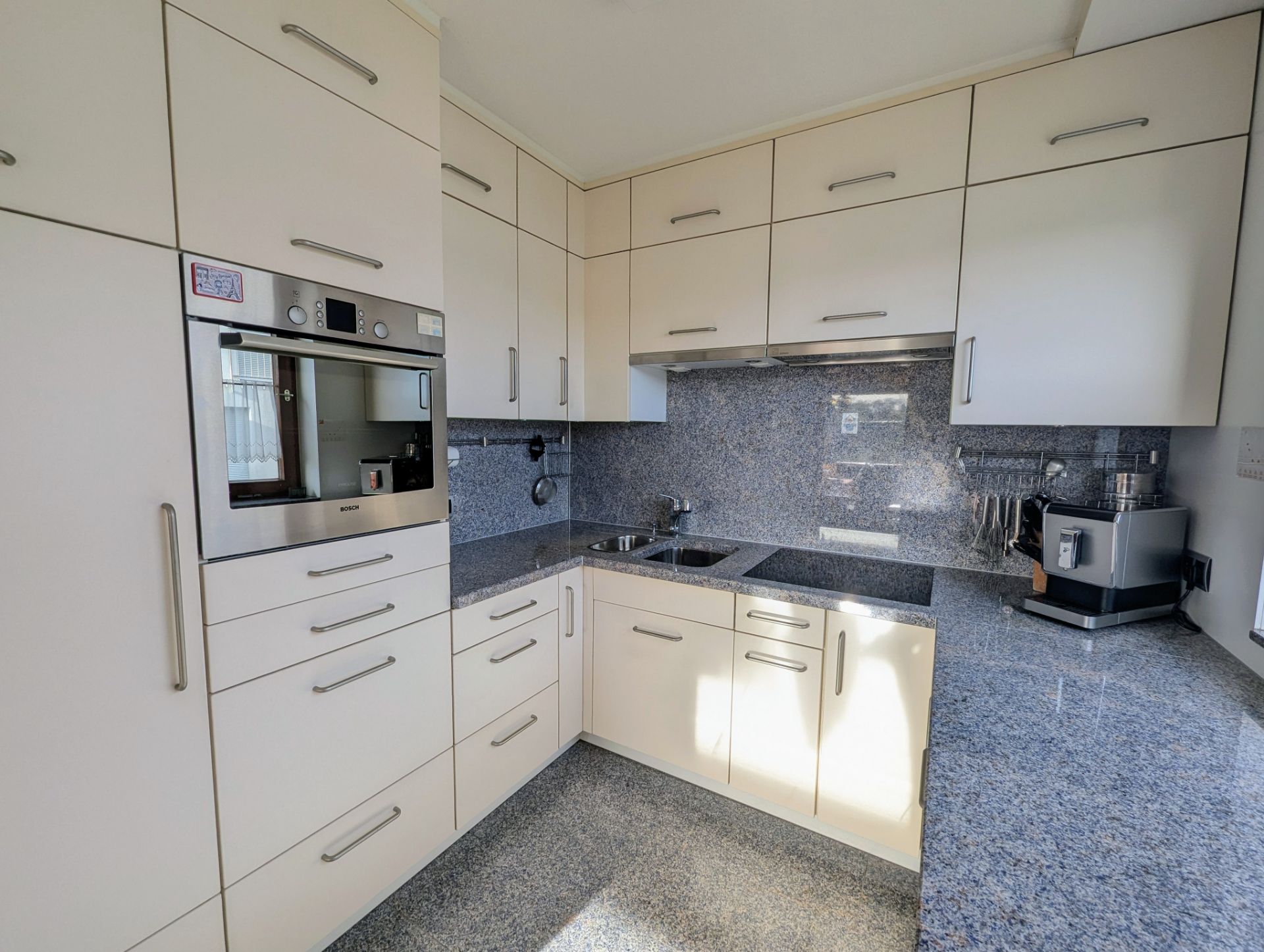 Moderne Einbauküche mit hellen Schränken, Backofen, Herd, Spüle und Kaffeemaschine.