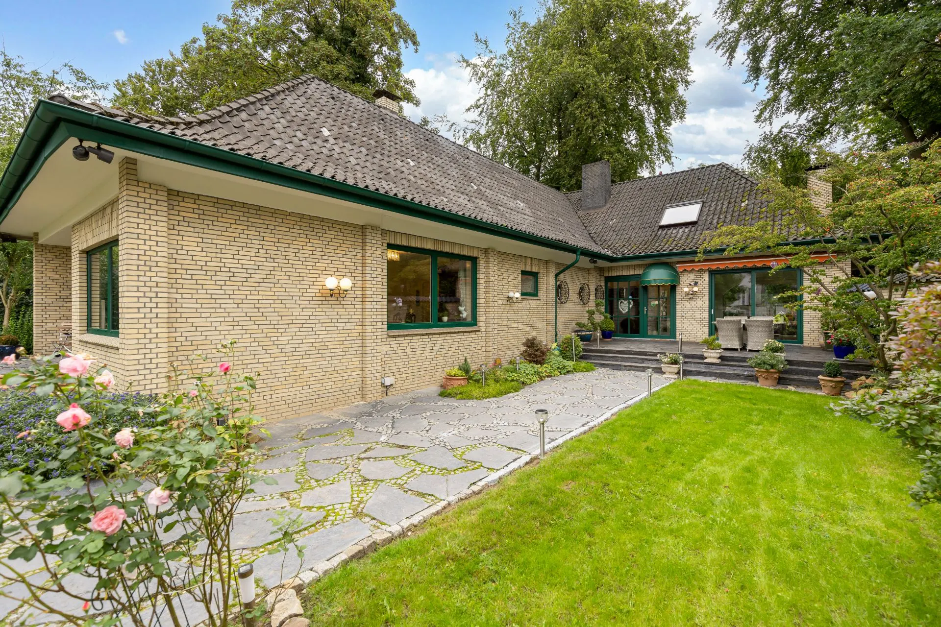 Einfamilienhaus mit hellem Mauerwerk, Garten, Terrasse und großem Fenster.