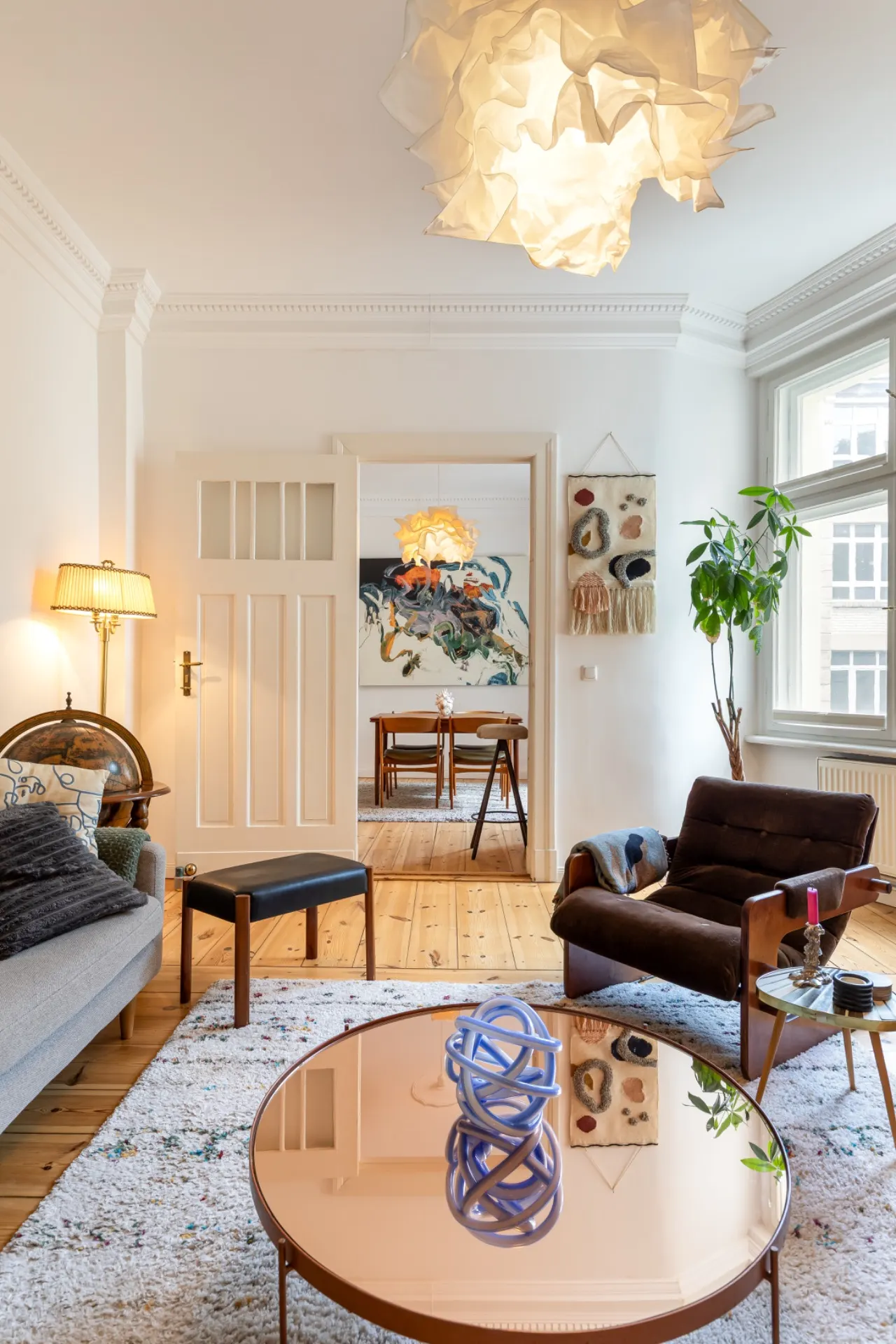Helles Wohnzimmer mit Sofa, Sessel, Couchtisch und großem Fenster, Blick ins Esszimmer.