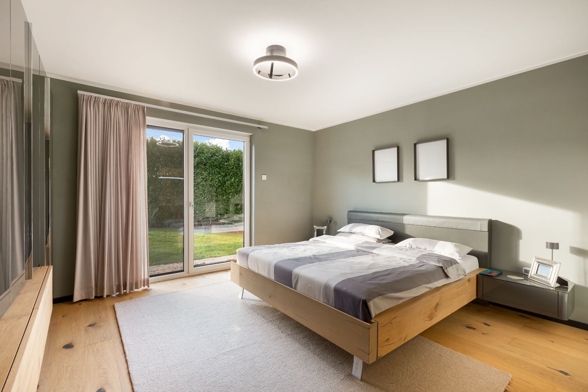 Helles Schlafzimmer mit Doppelbett, großem Fenster, Vorhängen und Holzfußboden.