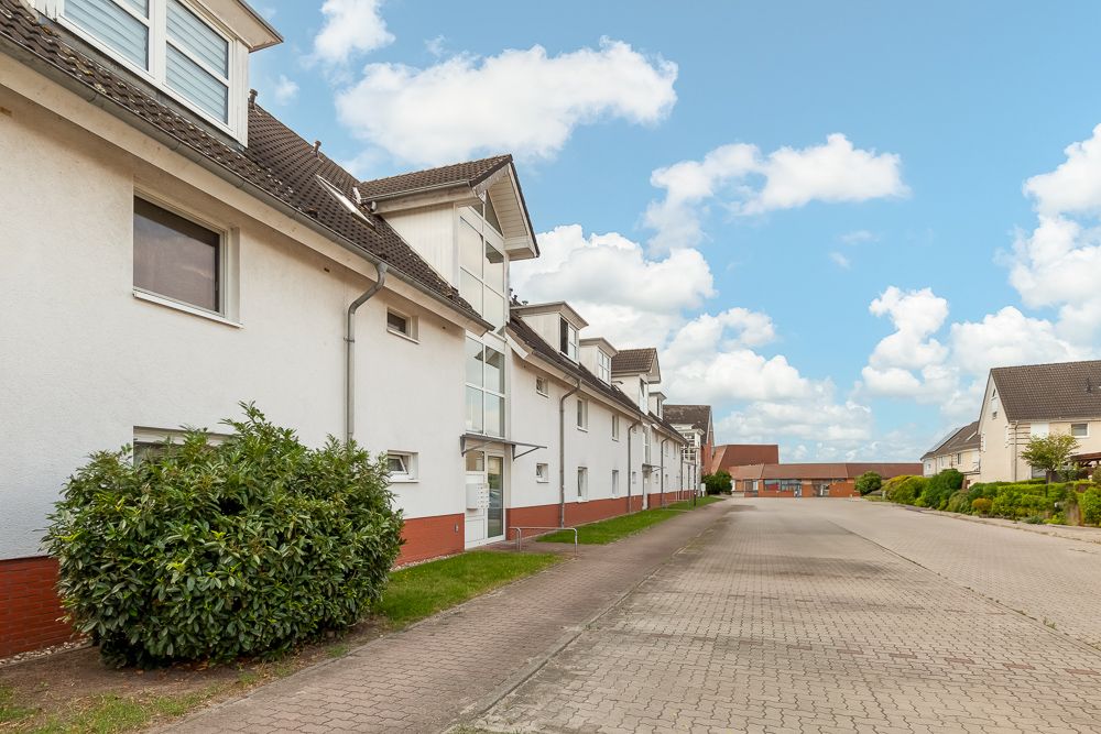 Weiße Wohnhäuser mit roten Sockeln und Vorgärten an einer gepflasterten Straße bei blauem Himmel.