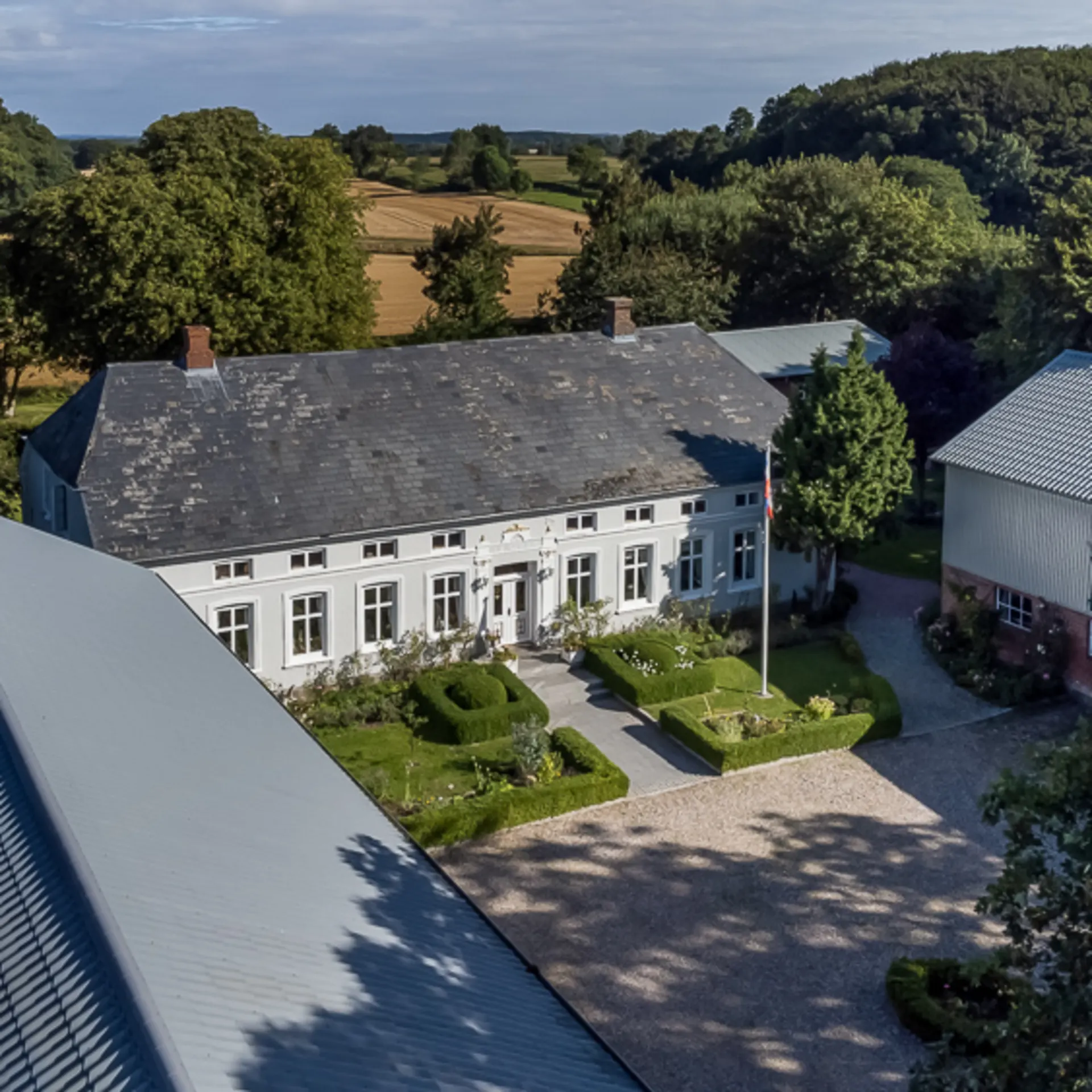 Luftaufnahme eines großen Wohnhauses mit Garten und Nebengebäuden, umgeben von Bäumen.