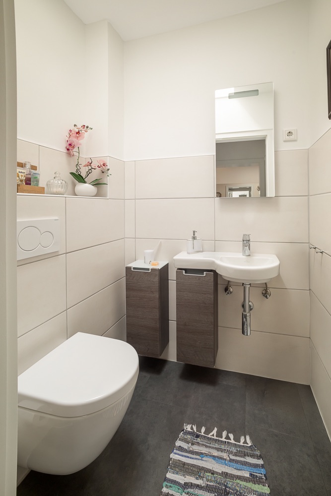 Modernes Badezimmer mit Toilette, Waschbecken, Spiegel und dekorativen Blumen.