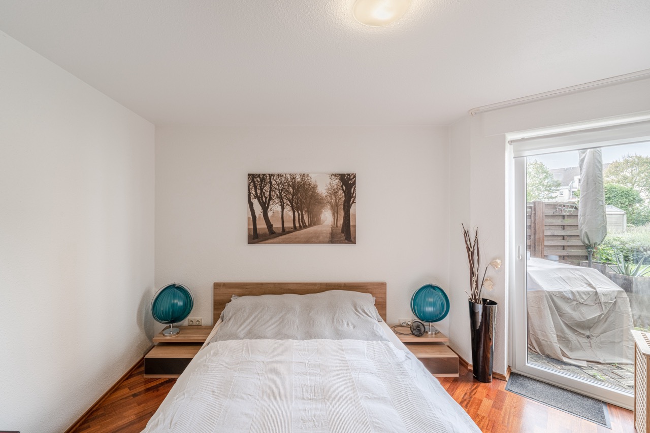 Schlafzimmer mit Doppelbett, zwei Nachttischen, Wandbild und Zugang zur Terrasse.