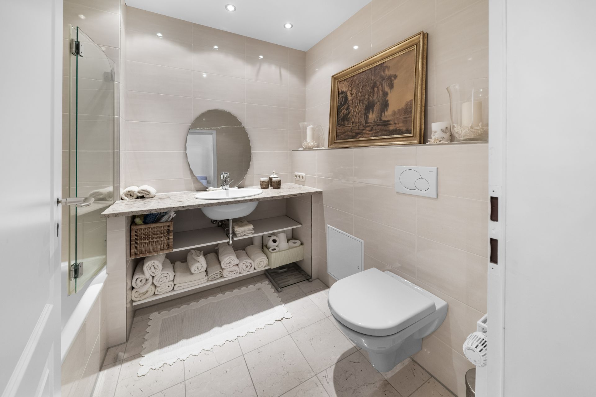 Modernes Bad mit Wandtoilette, Waschbecken, Spiegel, Dusche und gerollten Handtüchern auf Regalen.