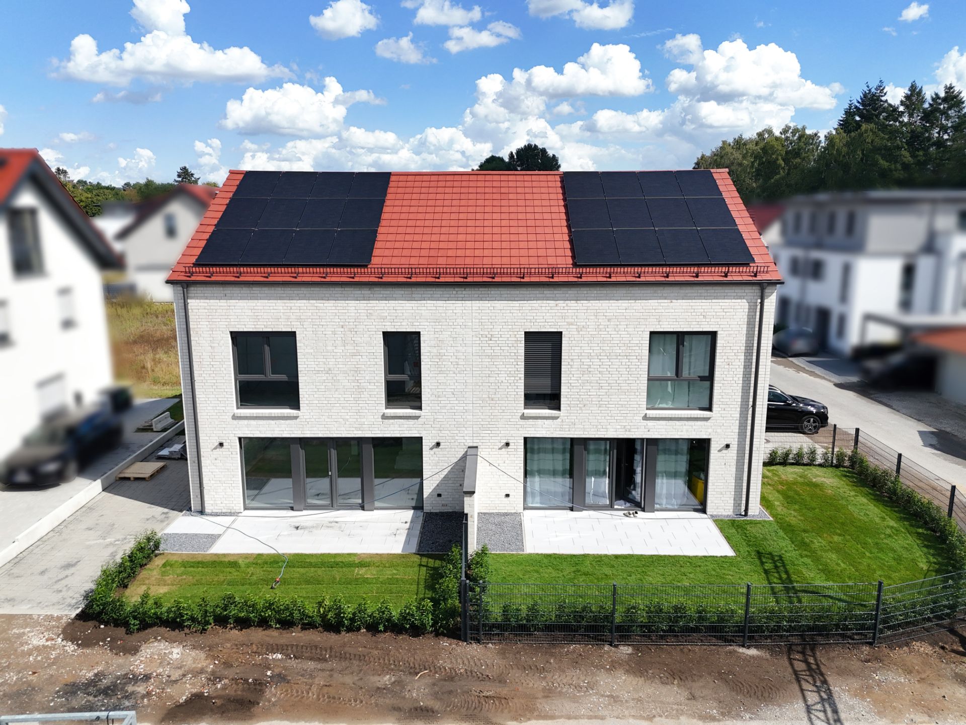 Modernes zweistöckiges Wohnhaus mit Solarpaneelen auf dem Dach und gepflegtem Garten.