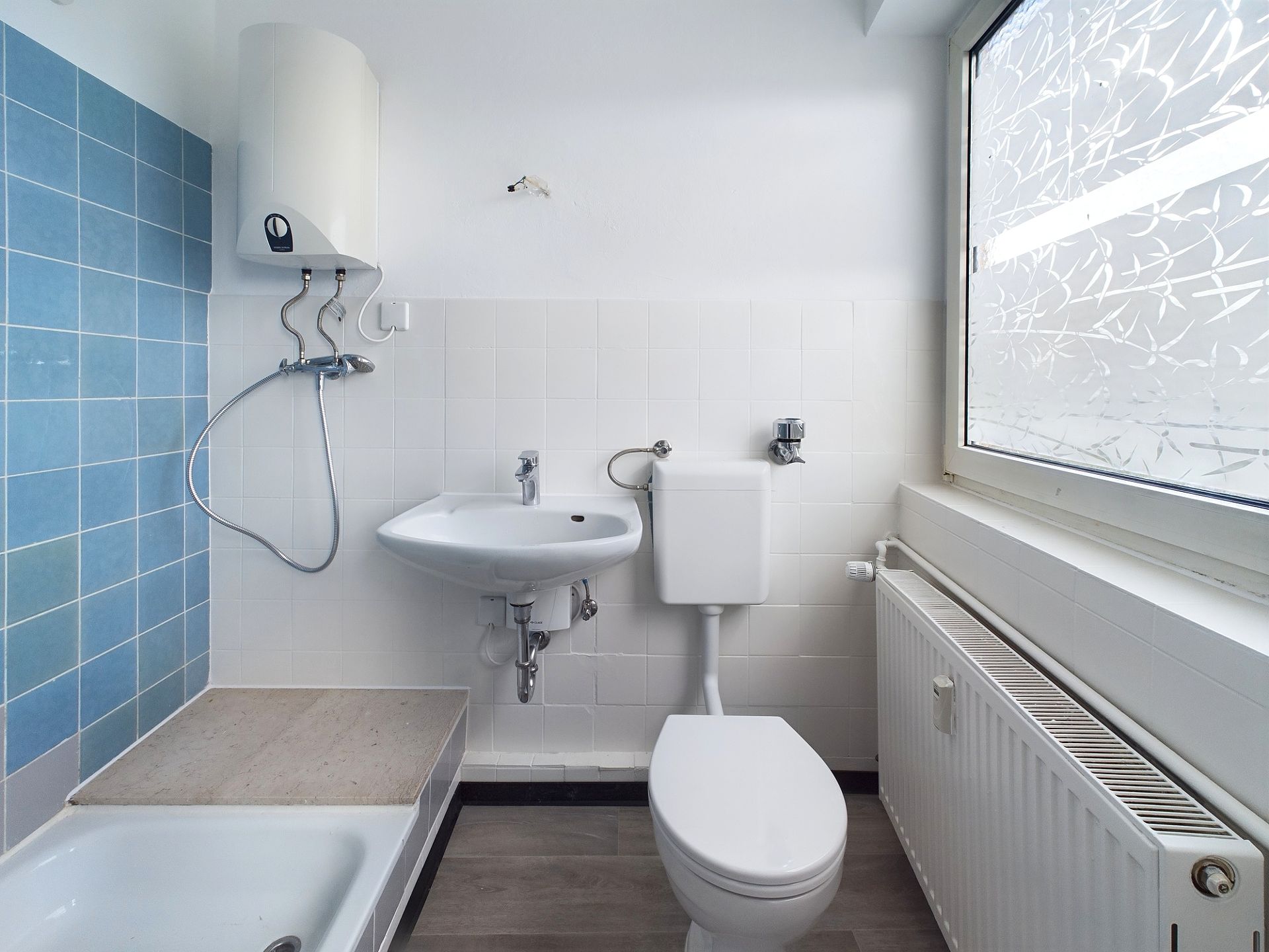 Kleines Badezimmer mit Toilette, Waschbecken, Dusche und großem Fenster.