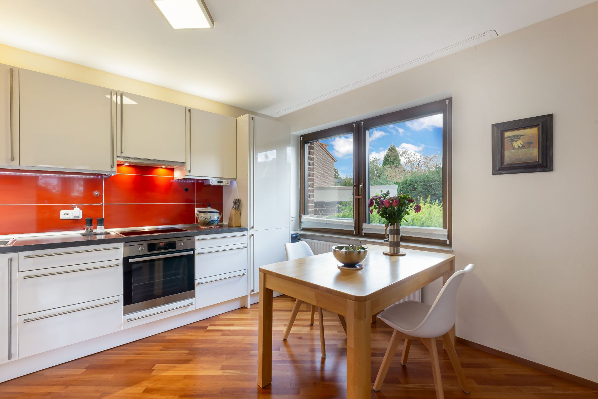 Moderne Küche mit Essbereich, Holzboden, Fenster und weiß-roten Möbeln.