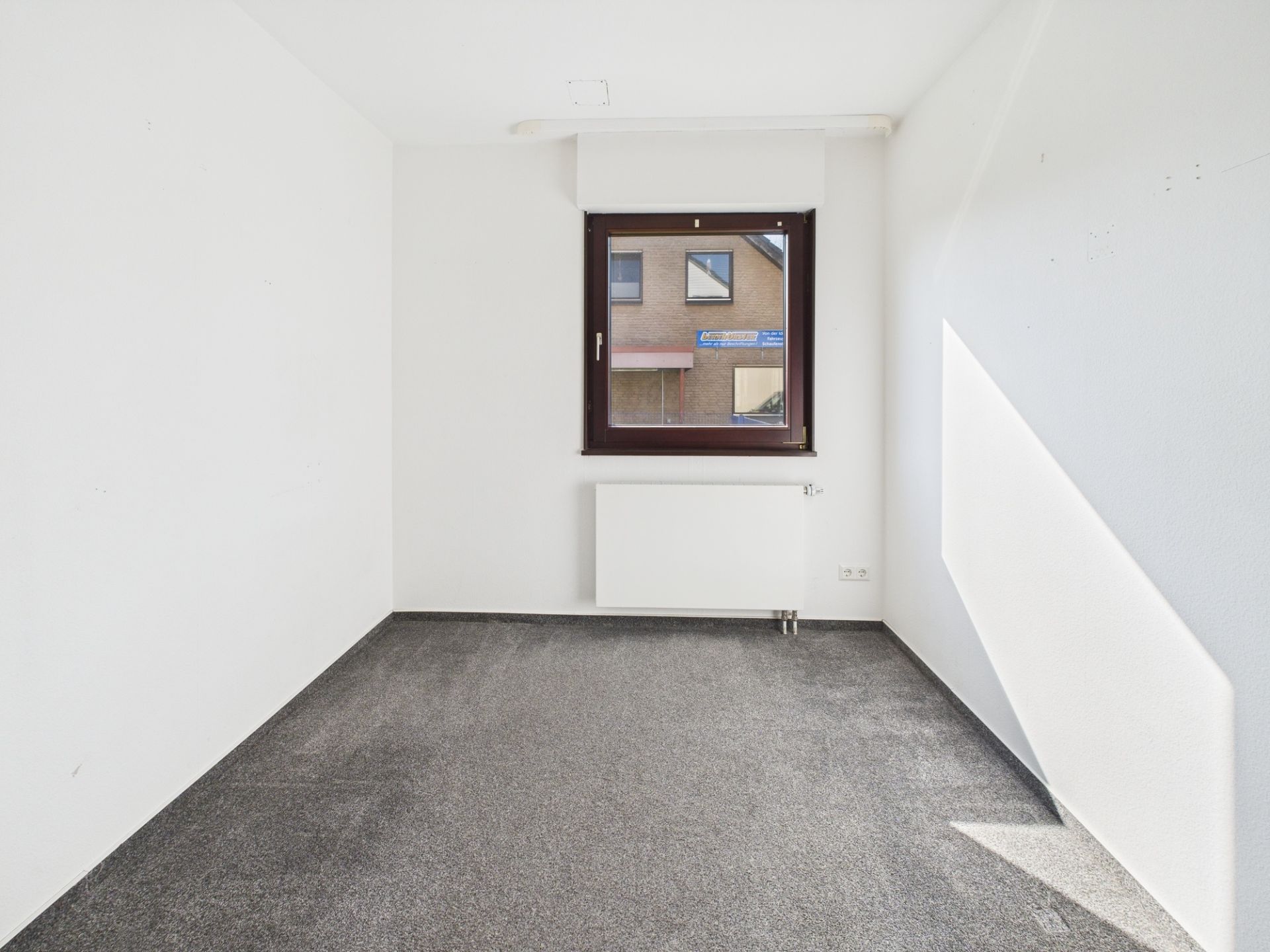 Leerer Raum mit grauem Teppich, weißem Heizkörper und Fenster.