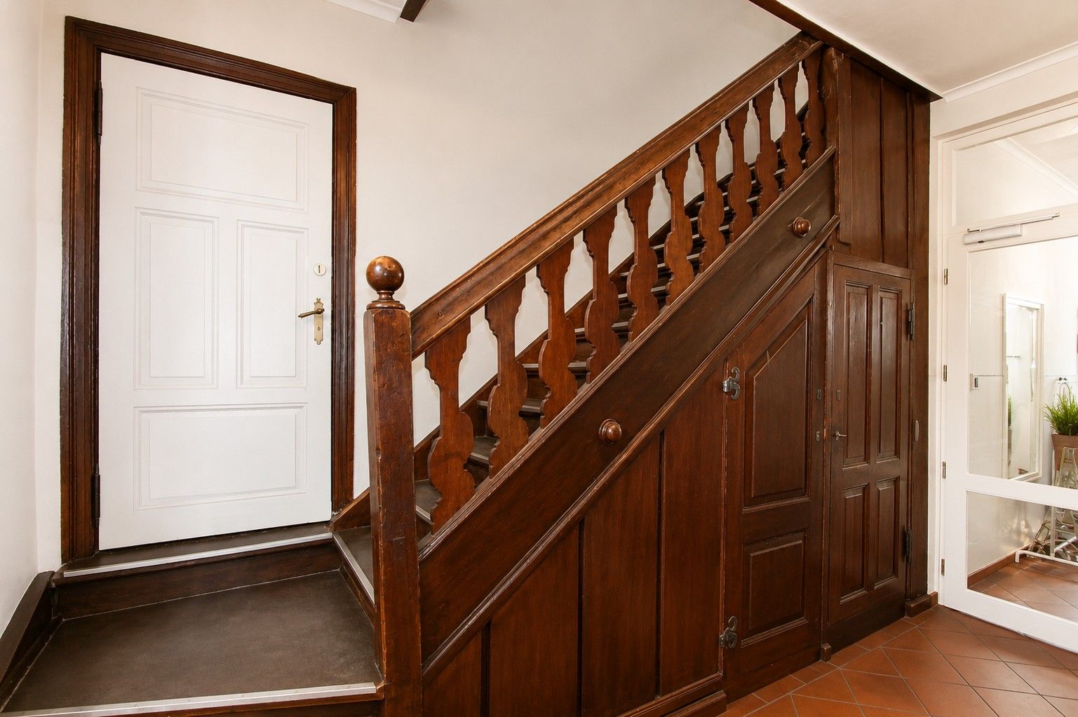 Flur mit hölzerner Treppe, weißer Tür und Einbauschrank unter der Treppe.