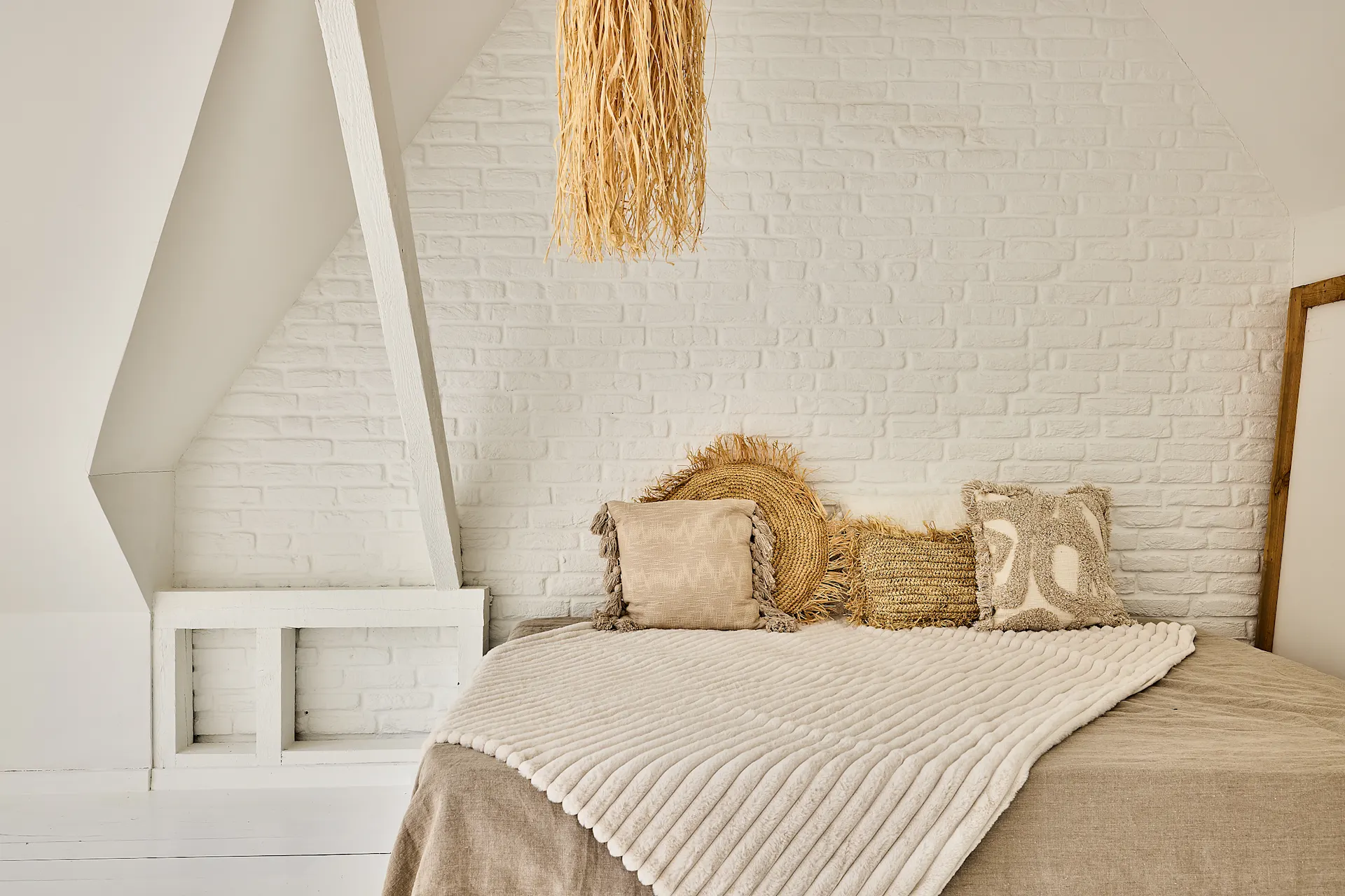 Gemütliches Schlafzimmer mit weißen Wänden, Bett und dekorativen Kissen in Naturtönen.