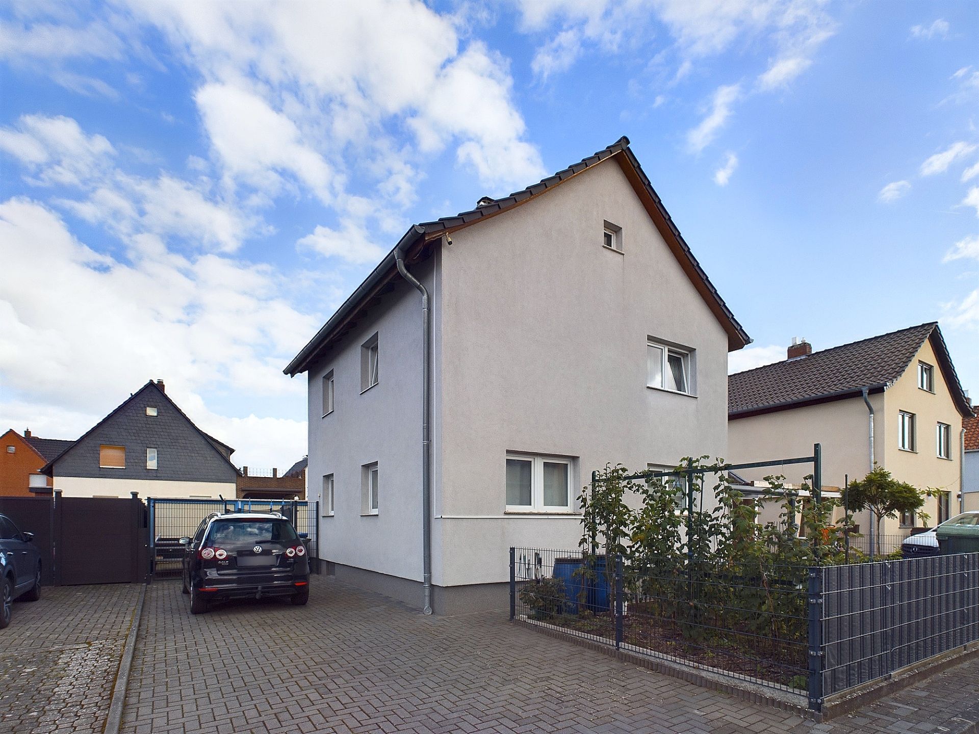 Zweistöckiges Wohnhaus mit weißer Fassade, Parkplatz und kleinem Garten, daneben weitere Häuser.