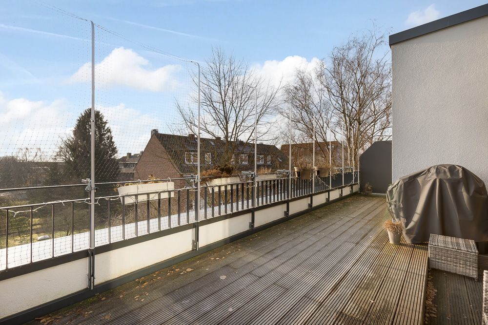 Große Holzterrasse mit Geländer, Netzschutz und Blick auf Nachbarhäuser und Bäume.
