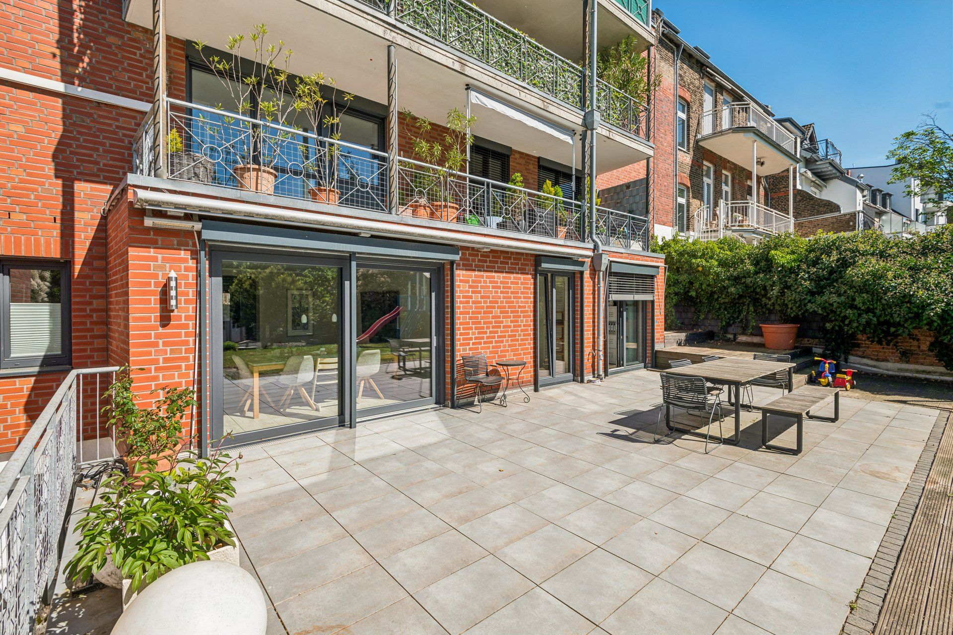 Große Terrasse mit Sitzbereich, Pflanzen und Zugang zu einer Wohnung in einem Mehrfamilienhaus.