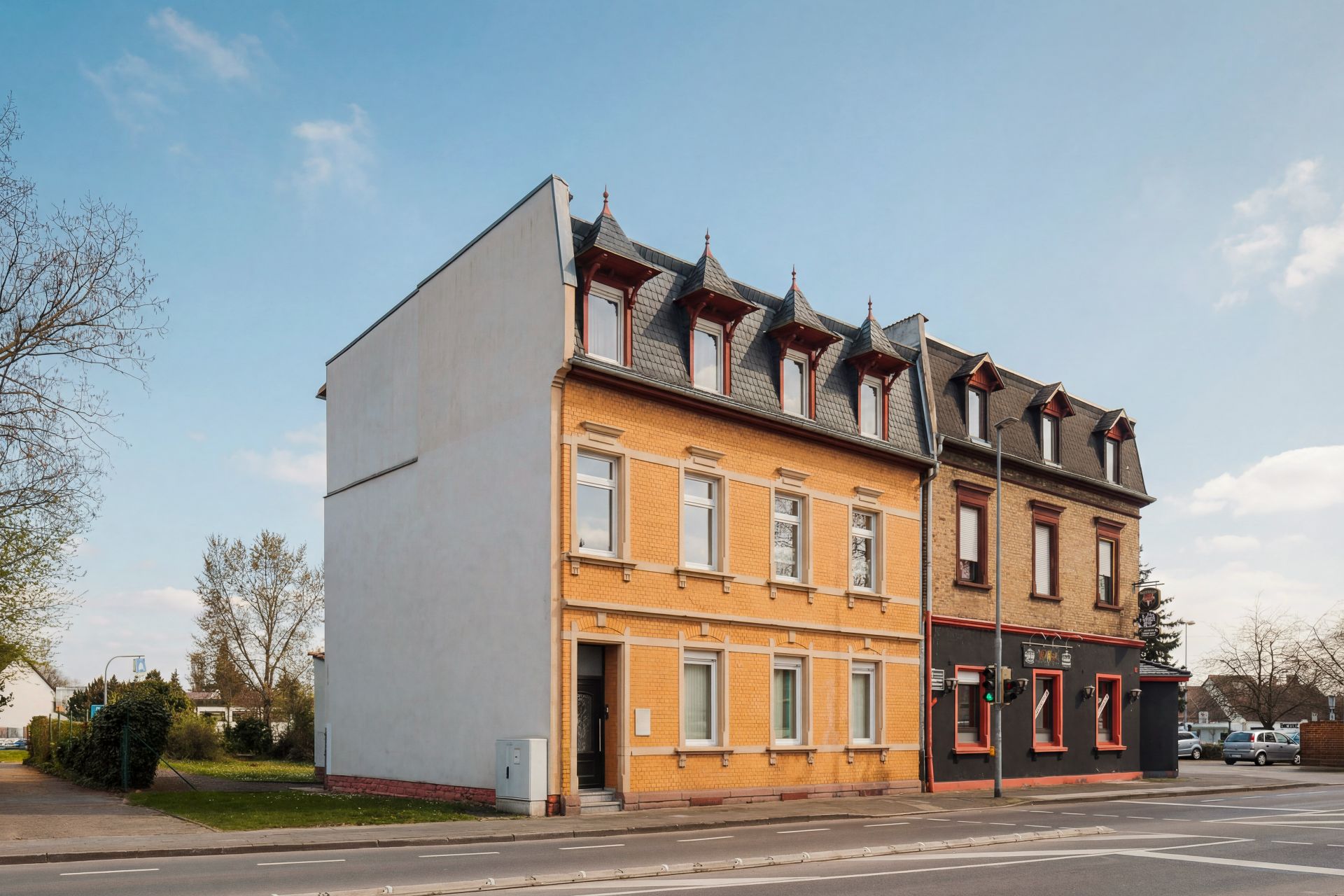 Zweistöckiges Wohnhaus mit gelber und brauner Fassade an einer Straße.