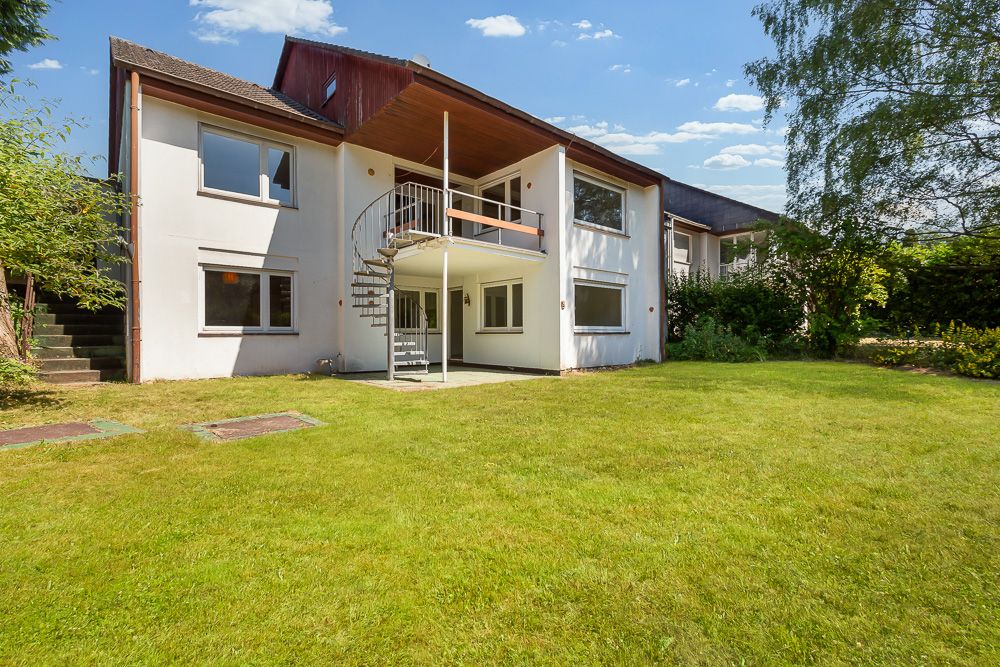 Zweistöckiges Wohnhaus mit Balkon, Wendeltreppe und großem Garten bei Sonnenschein.