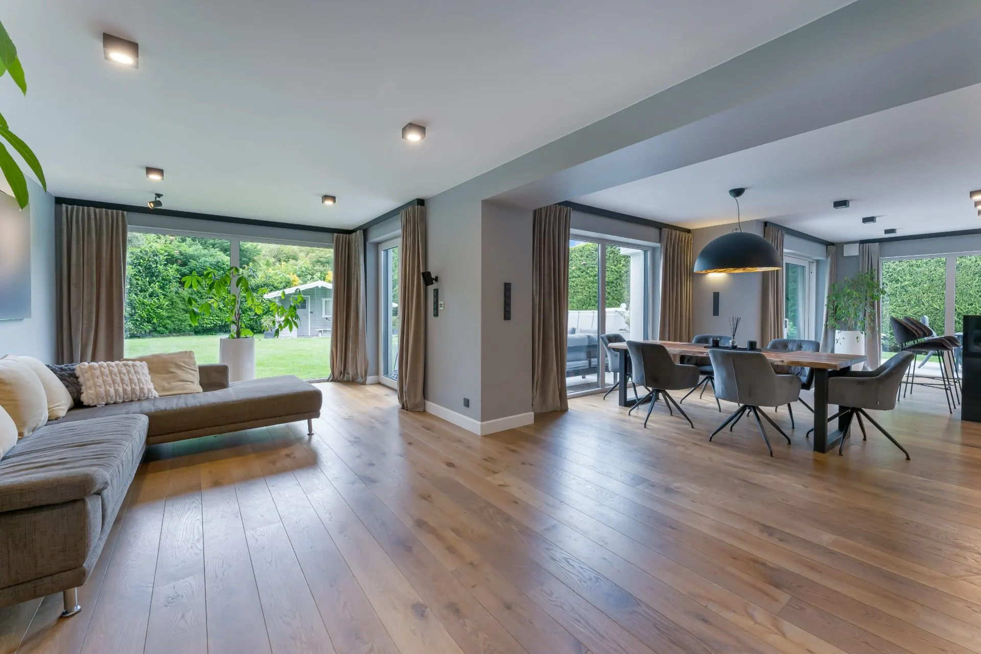 Modernes Wohnzimmer mit Essbereich, Holzboden, großen Fenstern und Zugang zum Garten.